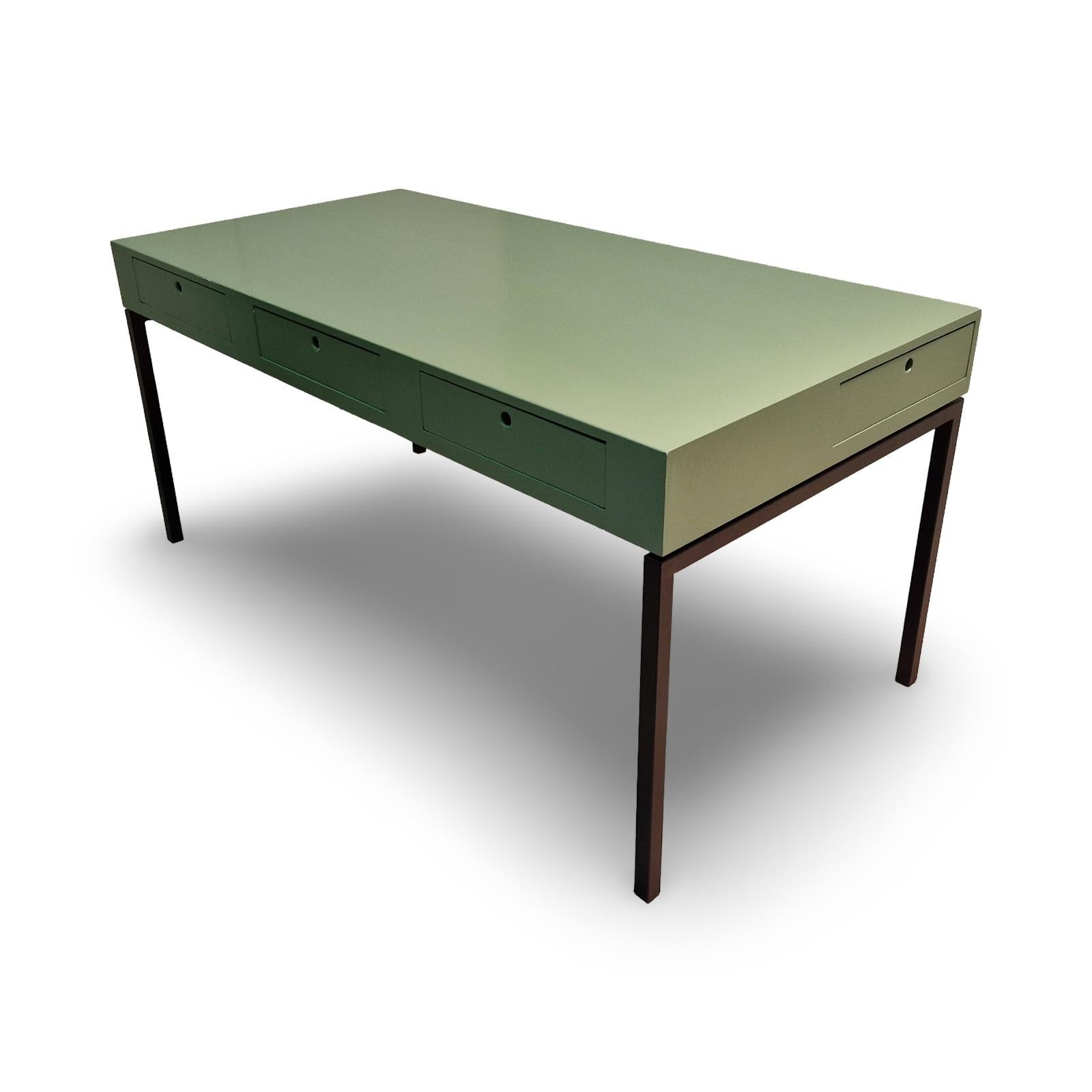 Escritorio de diseño minimalista. La parte superior es de madera maciza y está pintada de verde. La parte superior tiene 5 cajones. 3 situados en la parte delantera y 1 a cada lado. El cajón central es el más profundo, mientras que los demás cajones