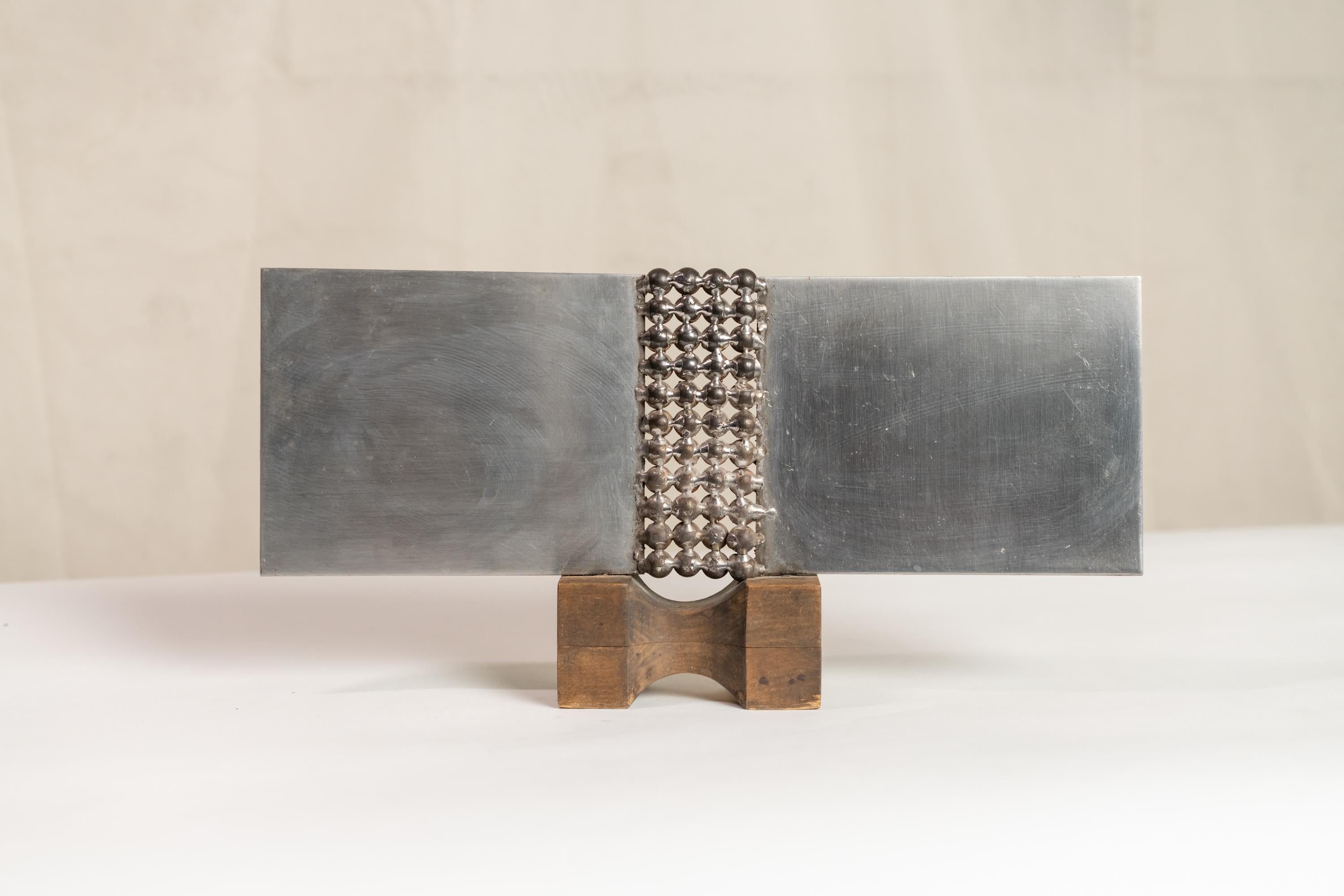 Modernist abstract polished steel sculpture resting on a wooden base. Sticker written: 