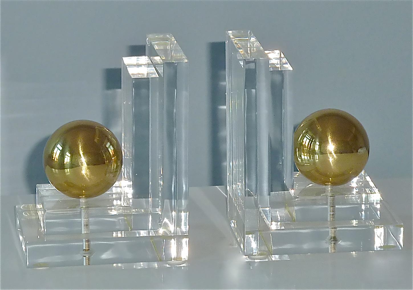 Sculptural pair of French or Italian acrylic lucite clear plastic bookends in Art Deco Style with patinated gilt brass globe balls, Italy or France around 1970s. The chic, elegant and timeless design of the bookends reminds works by Gabriella Crespi