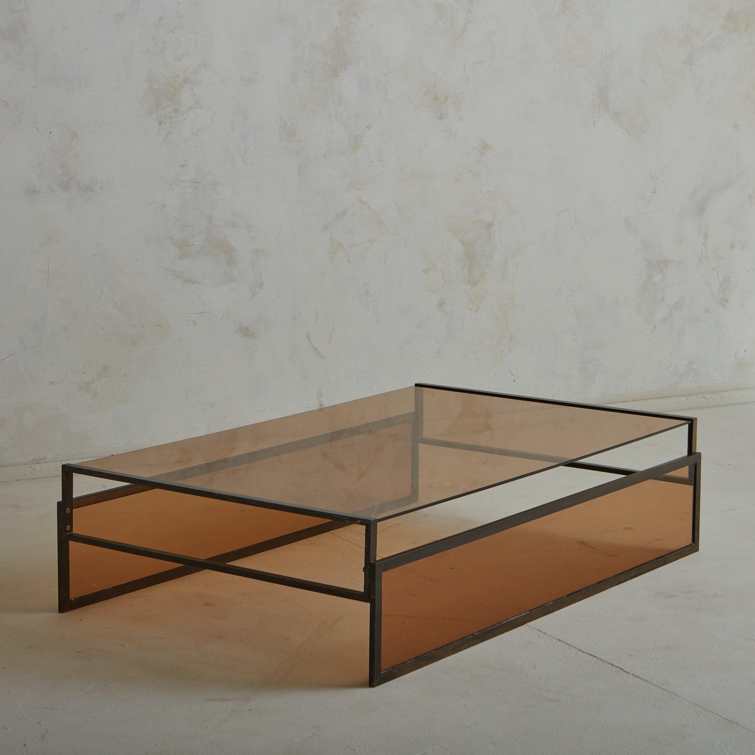A vintage French coffee table featuring a rectangular patinated iron block frame with an inset amber glass tabletop. Matching amber glass pieces partially line two sides of the table, which emphasize the angular lines and highlight the table’s