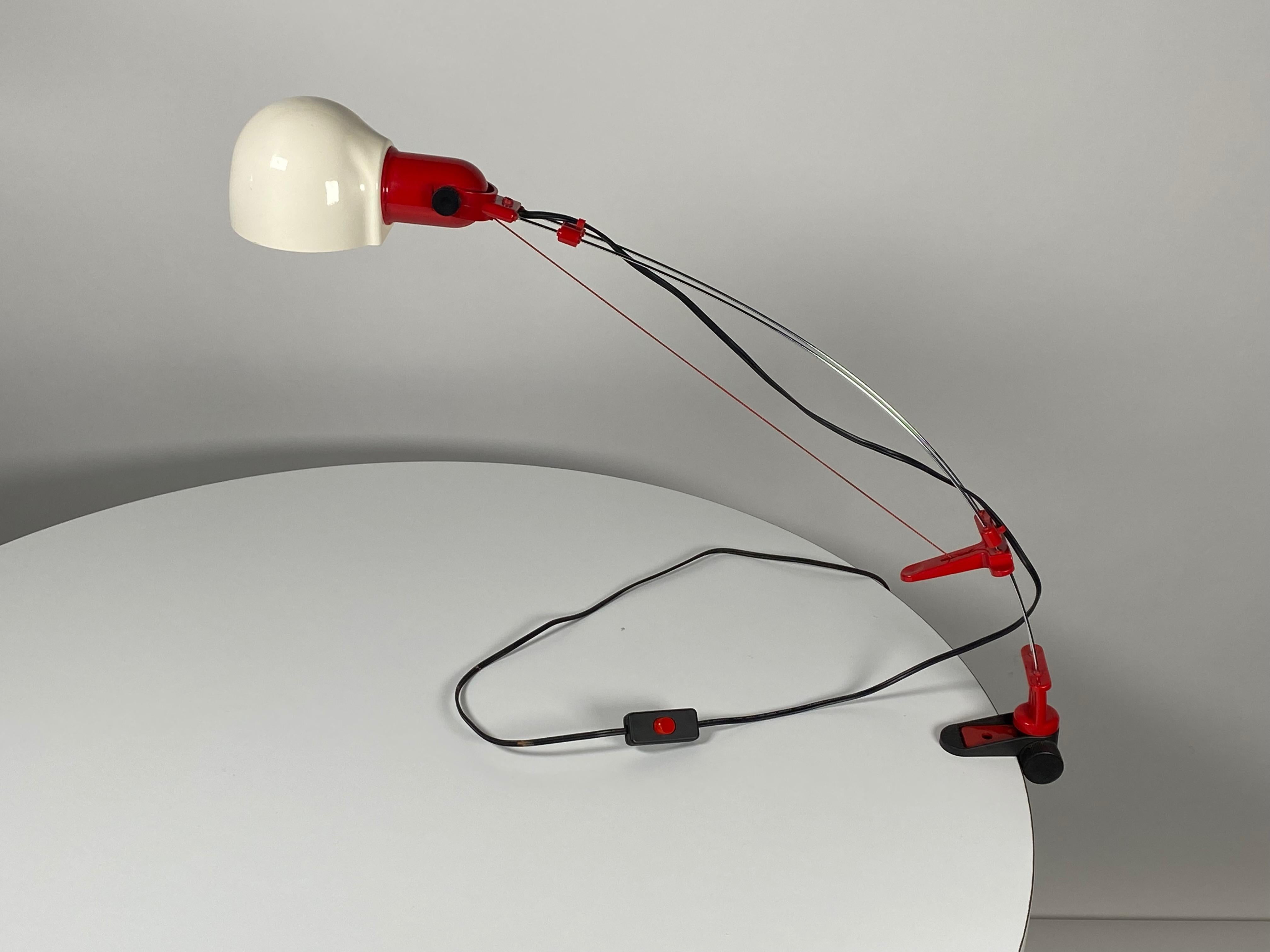 Post Modern design in this clamp desk lamp chromed wire architecture with a cord tension for adjusting the height. Constructed of red and white plastic, the shade also adjusts which can be turned for light direction.