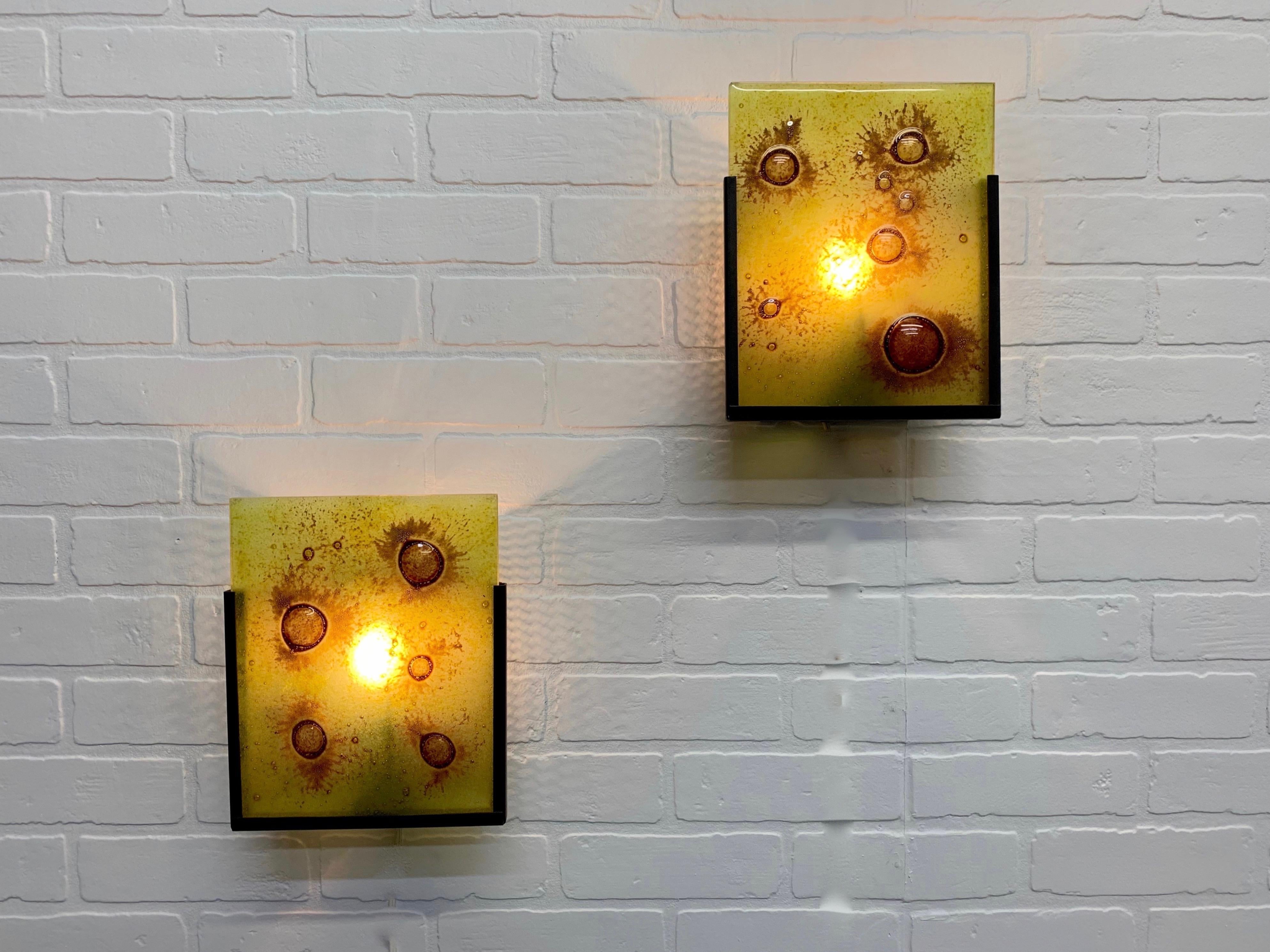 Pair of bronze powder-coated perforated wall mount with art glass panel that slips into the front and illuminated from the rear by single light bulb.