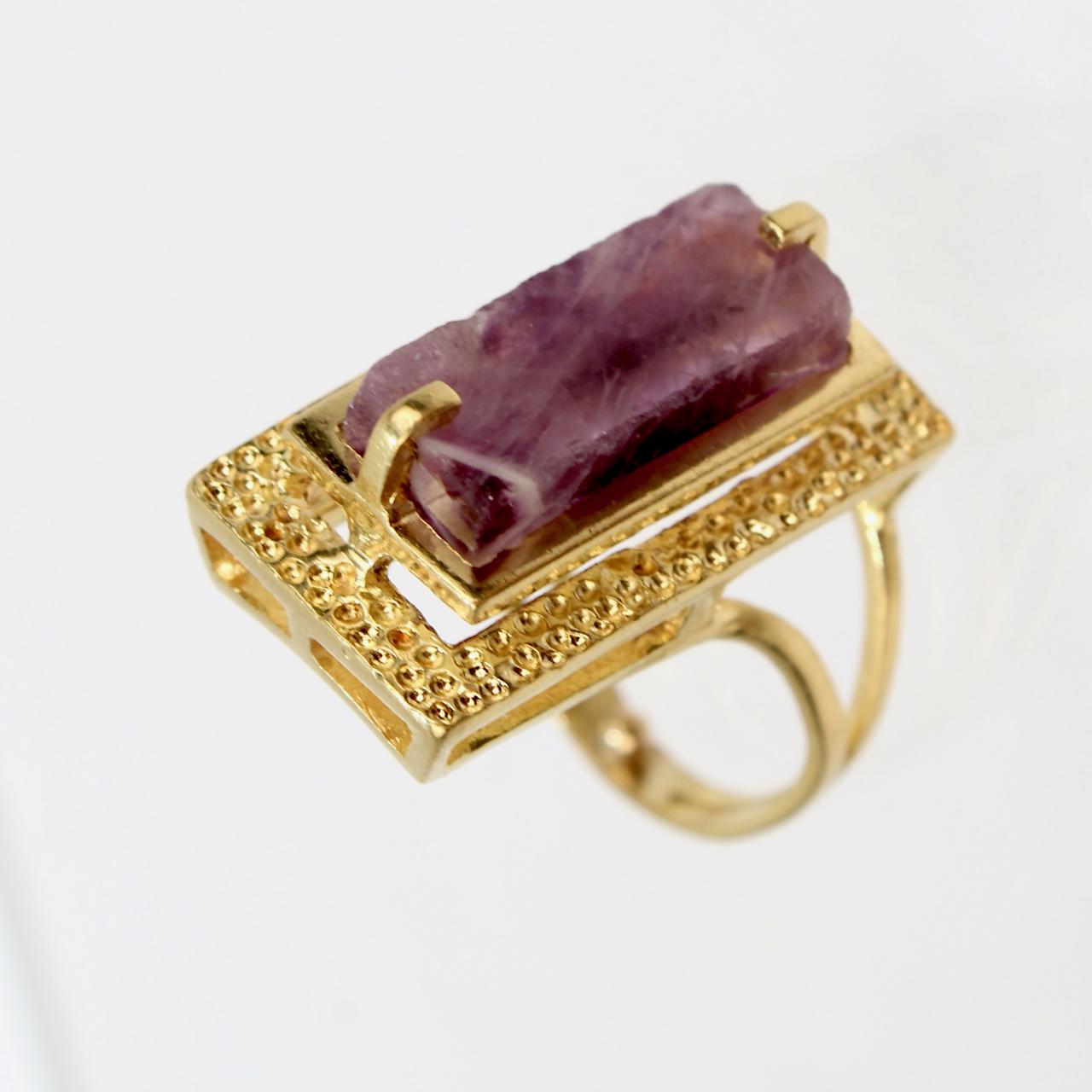 A very fine 18k gold and amethyst modernist cocktail ring.

With a rectangular cut amethyst gemstone prong set above a stippled and hammered platform setting that is supported by an asymmetrical split shank.

Very cool mid-century