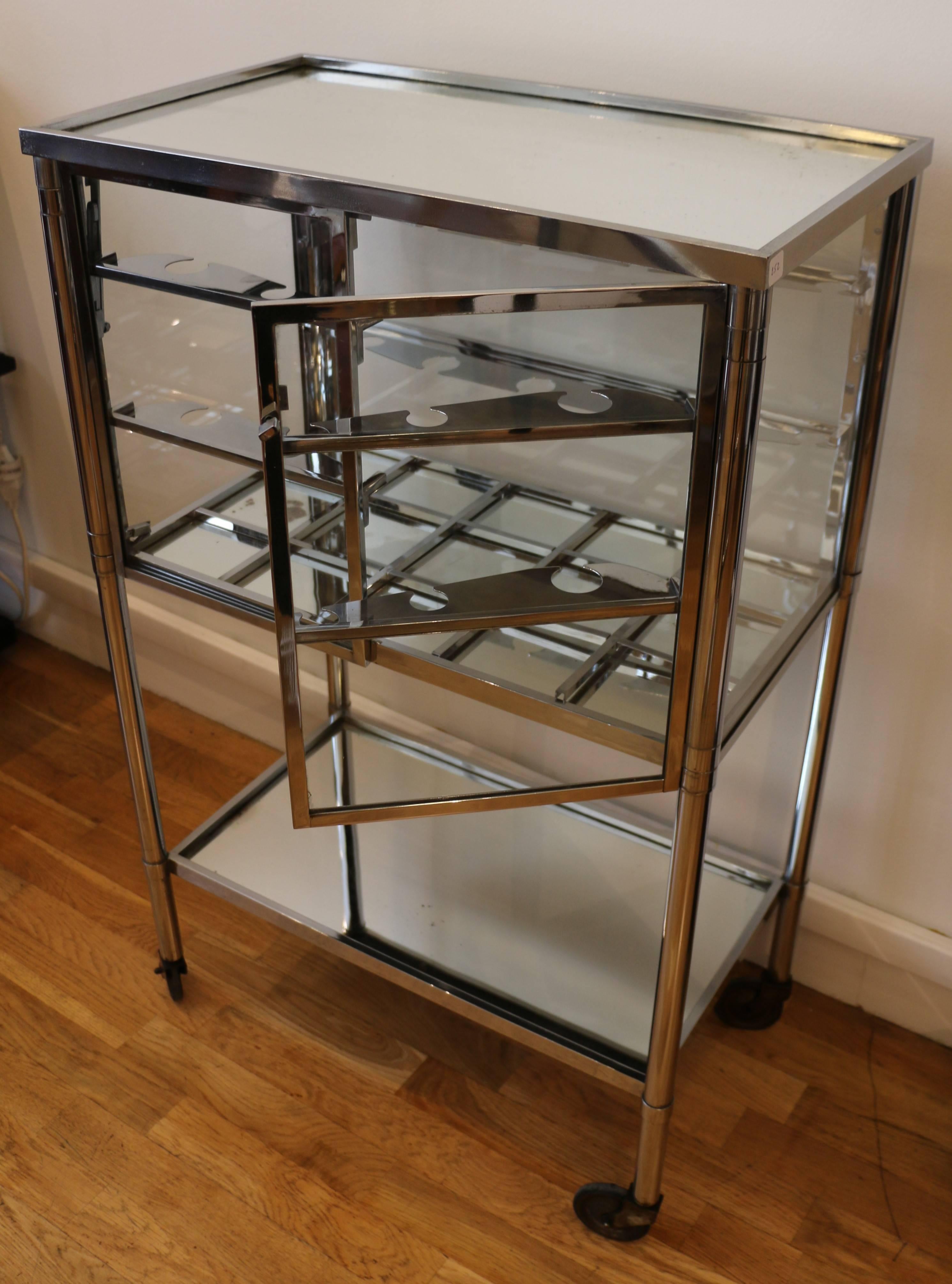 Bar cart on wheels by Jacque Adnet (1900-1984). Modernist style. Frame in Chromium plated metal, glass and mirrors. Two front doors, the two sides can be lifted to increase the size of the top. Top, middle and bottom shelves made of mirrors. Glass