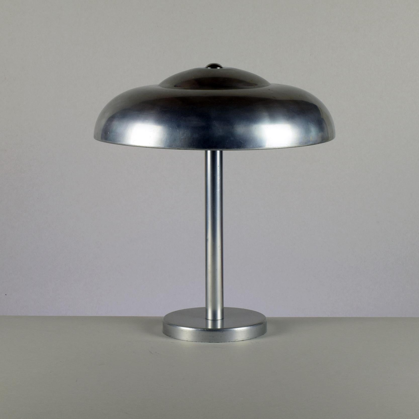 Una hermosa lámpara de aluminio para escritorio o mesa, de hacia 1930.
Exquisitamente fabricada con preciosos detalles, es una de las más elegantes de este estilo de lámpara de escritorio que hemos visto.

Aunque todavía no hemos podido atribuir