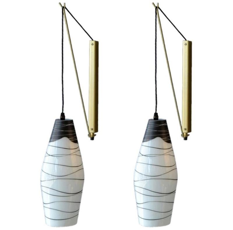 Pairs of wall-mounted pendants with opal shades hand painted in black hanging of black braided flex on an adjustable bronzed metal bracket. The height of the flex can be adjusted and the metal bracket allows the lamps to hang closer or further away