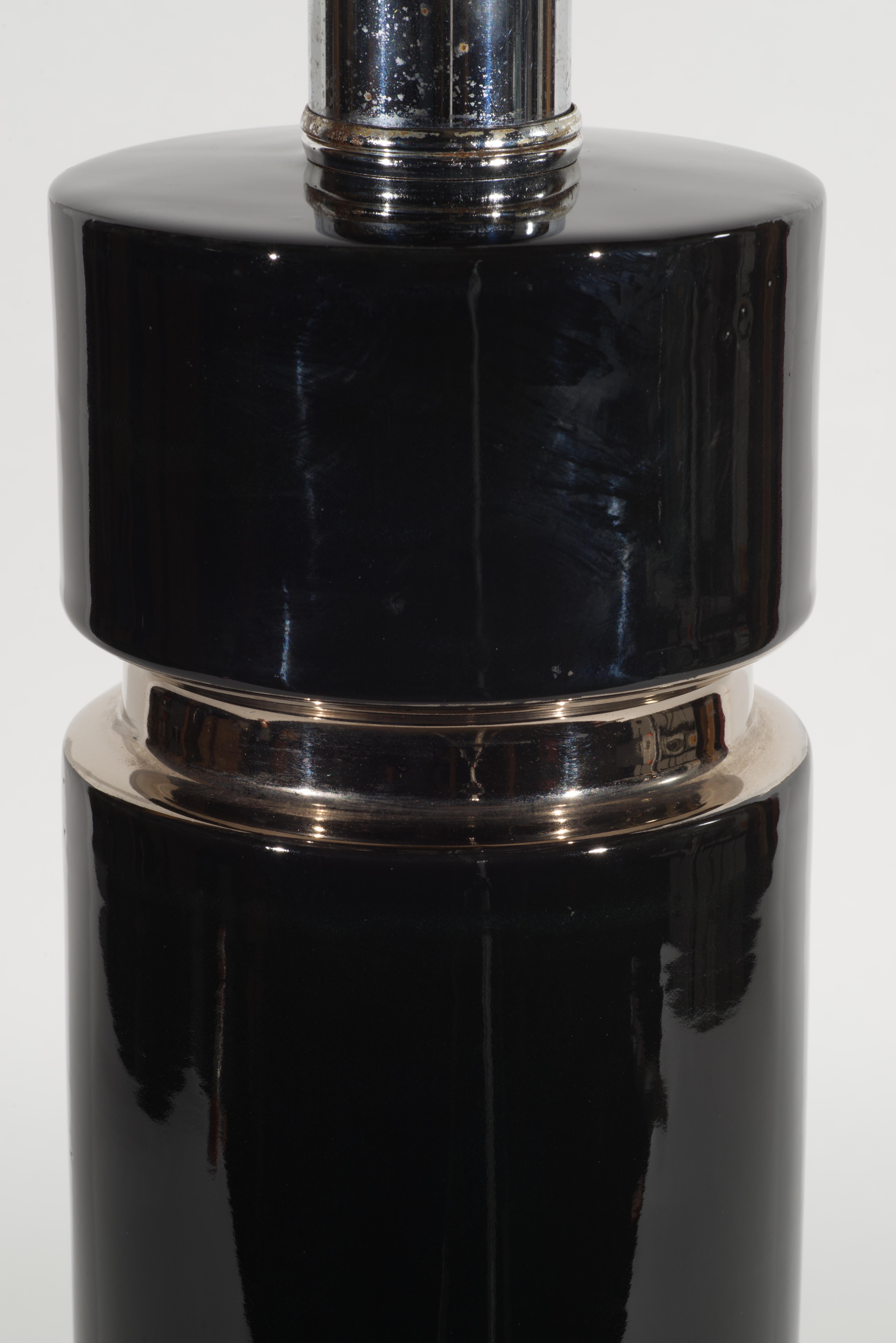  Lampe de table vintage en céramique de grande taille avec un corps cylindrique en forme de colonne et un large bandeau. La lampe est décorée d'une glaçure noire monochromatique brillante et d'un bandeau platine appliqué. La forme épurée de la