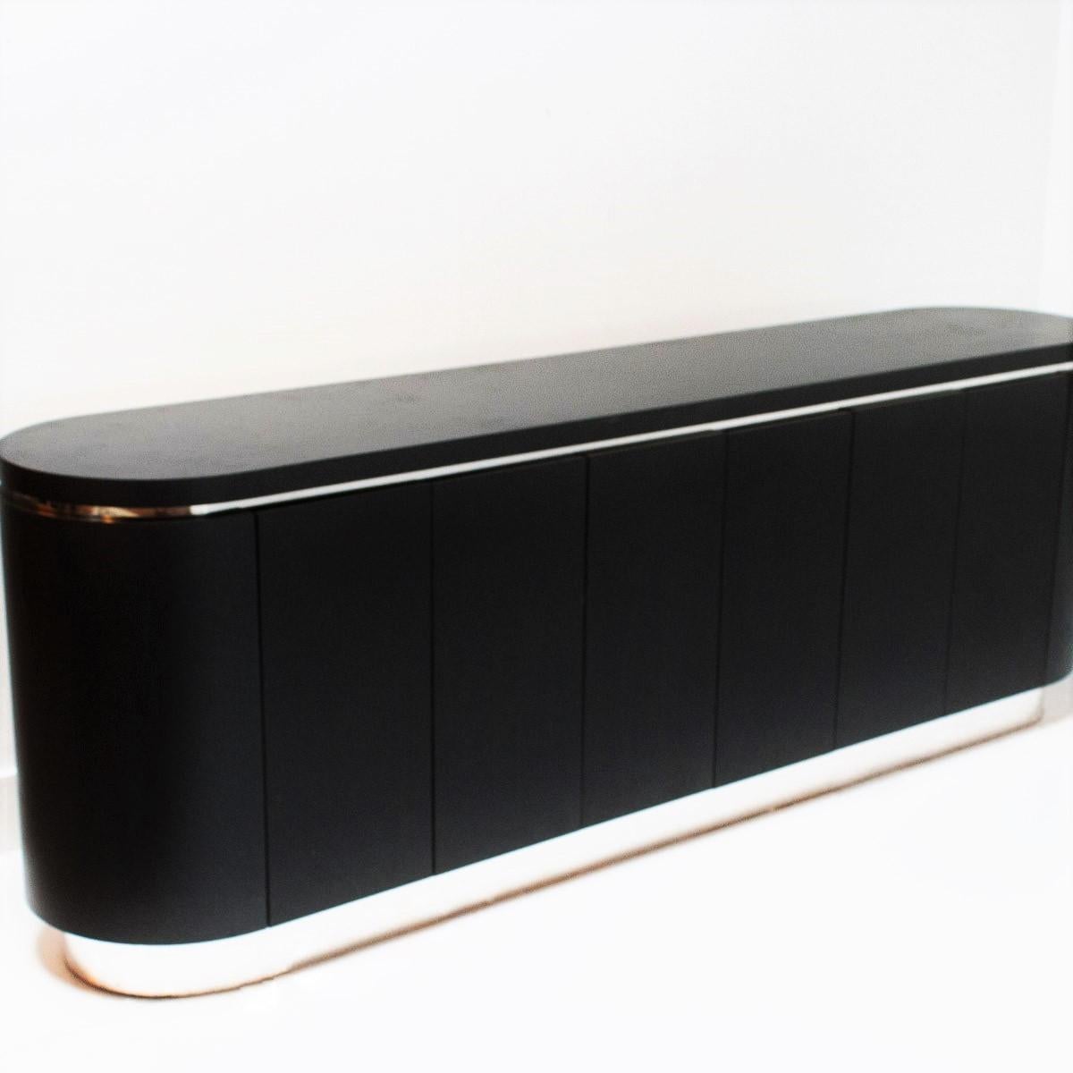 Exceptional proportions, black lacquered credenza with rounded ends. Consist of three double doors that hide internal shelves. Chrome strip inset between the top and cabinet, resting on a chrome plinth base.