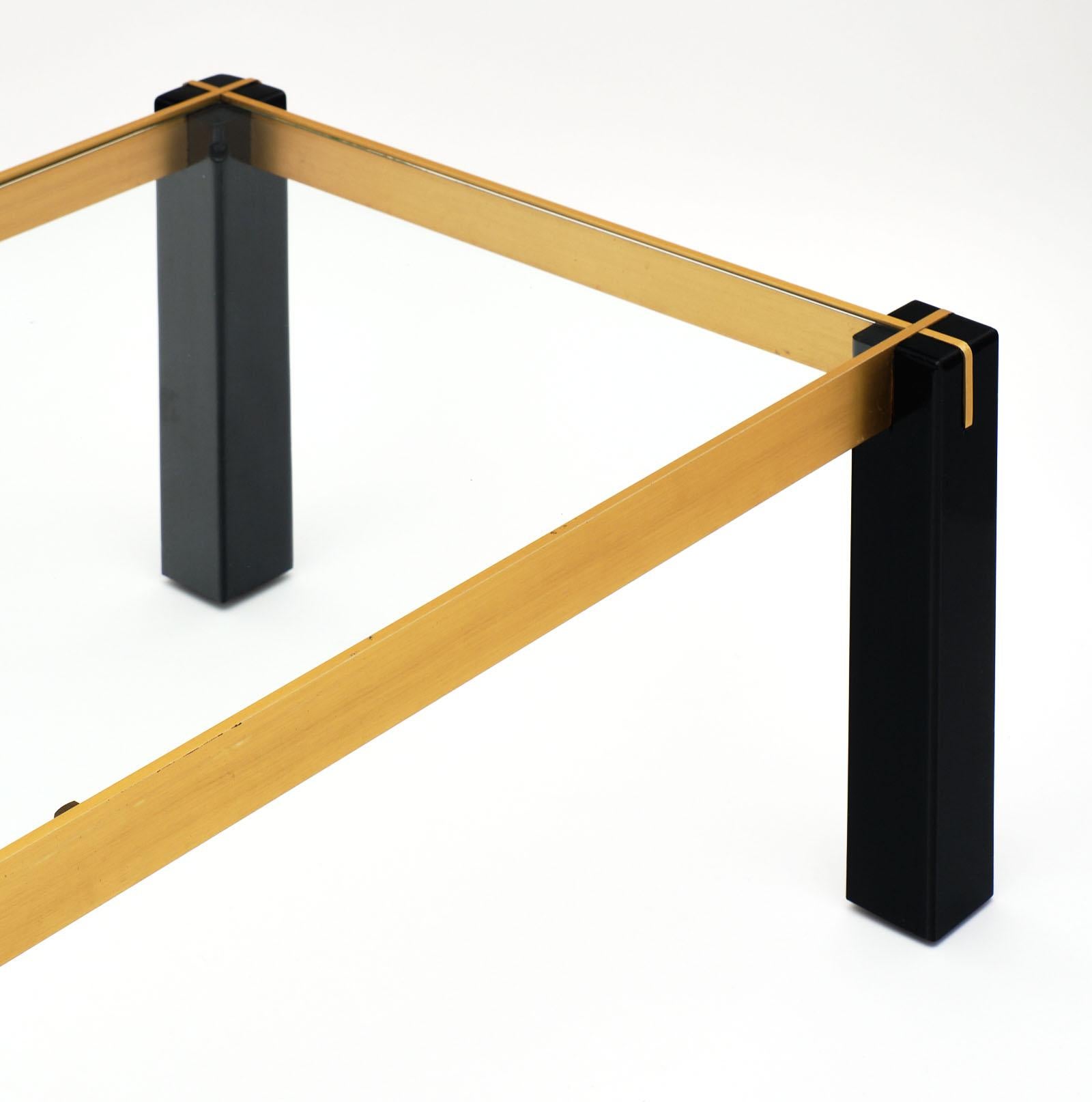 A rectangular French modernist brass and black coffee table with square section legs and clear glass, inserted on the top in the brass metal structure, which makes an x shape on each leg. We love the combination of brass with the black ebonized legs.