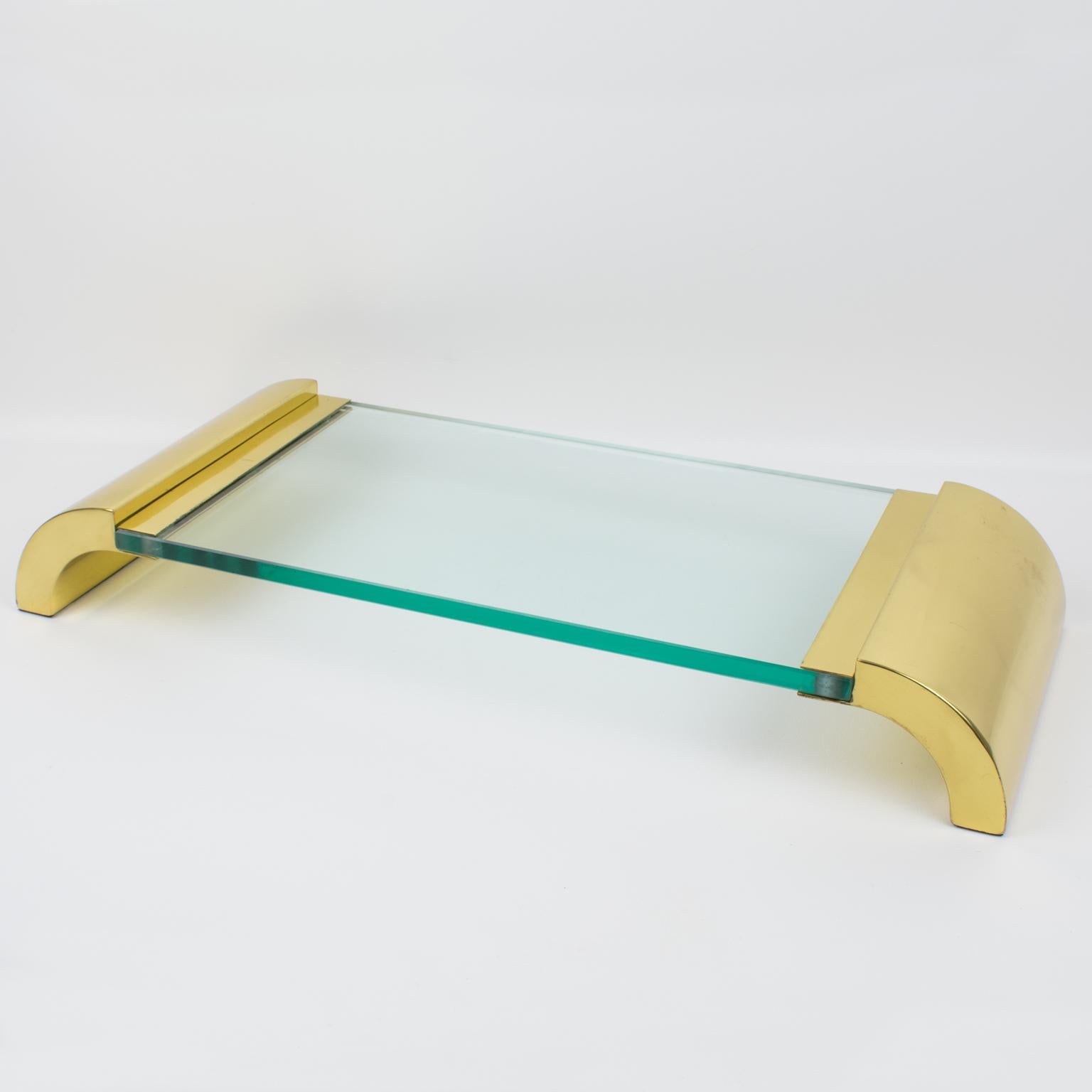 Este precioso centro de mesa o bandeja expositora de latón y cristal fue diseñado y fabricado en Italia hacia 1980. La pieza de presentación tiene un diseño modernista y minimalista con laterales macizos de latón pulido en relieve, complementados