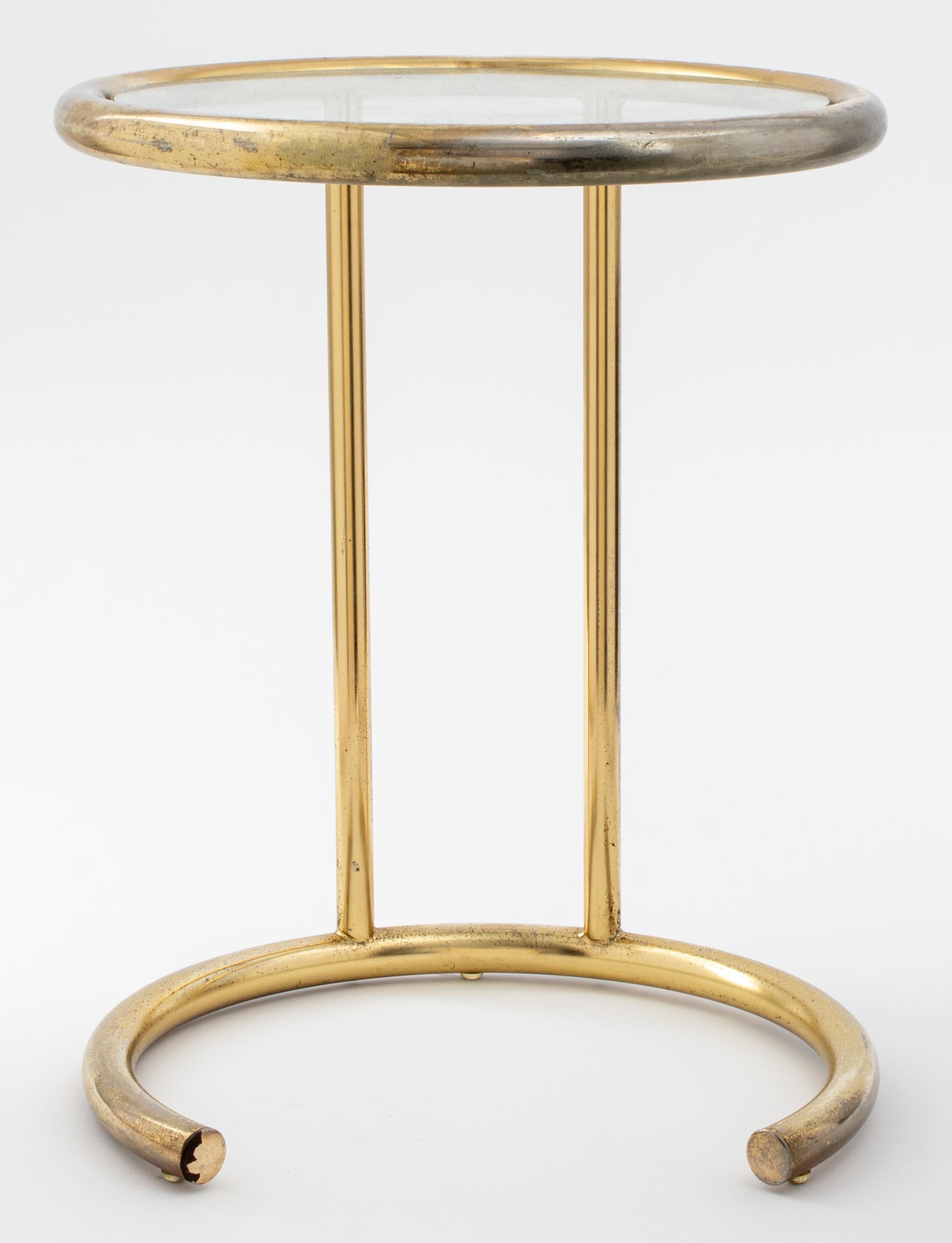 Modernist brass and glass round tubular side table in the manner of Eileen Gray, the round top with glass inset supported on one side by two uprights and c-shaped open tubular base. 
Measures: 18.75