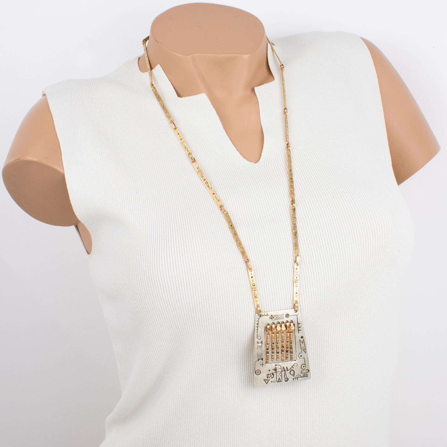 This amazing artisan studio modernist brass and silvered metal link necklace was created in the 1960s. The piece features a long brass link chain ornate with a silvered and brass metal pendant with dangling charms. The necklace has a handmade feel