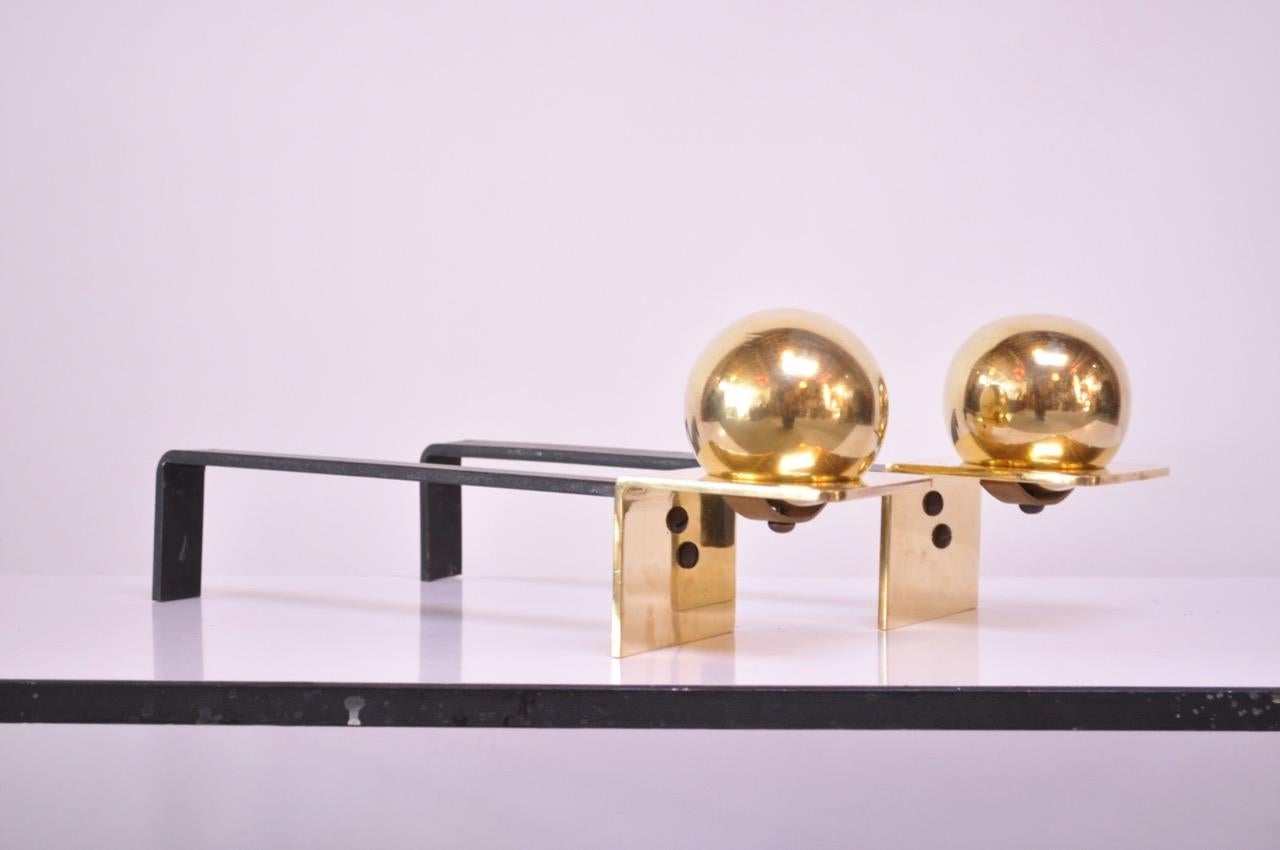 Pair of brass and iron andirons featuring a 'ball' or 'orb' decoration, each supported by a brass upright, all attached to an iron billet bar. Brass has been polished but light wear remains (unevenness to finish in place, light scuffs, few