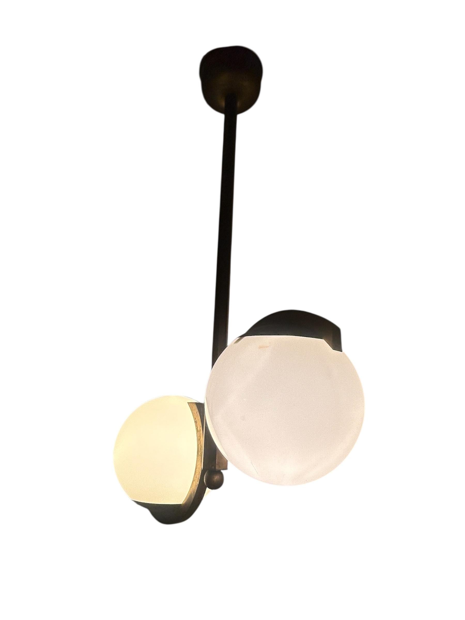 Una sublime lámpara Art Déco de estilo modernista, que combina la elegancia arquitectónica con los materiales nobles. Su marco de latón macizo finamente elaborado ofrece una presencia cálida y atemporal. Equilibra dos globos opalinos, difundiendo