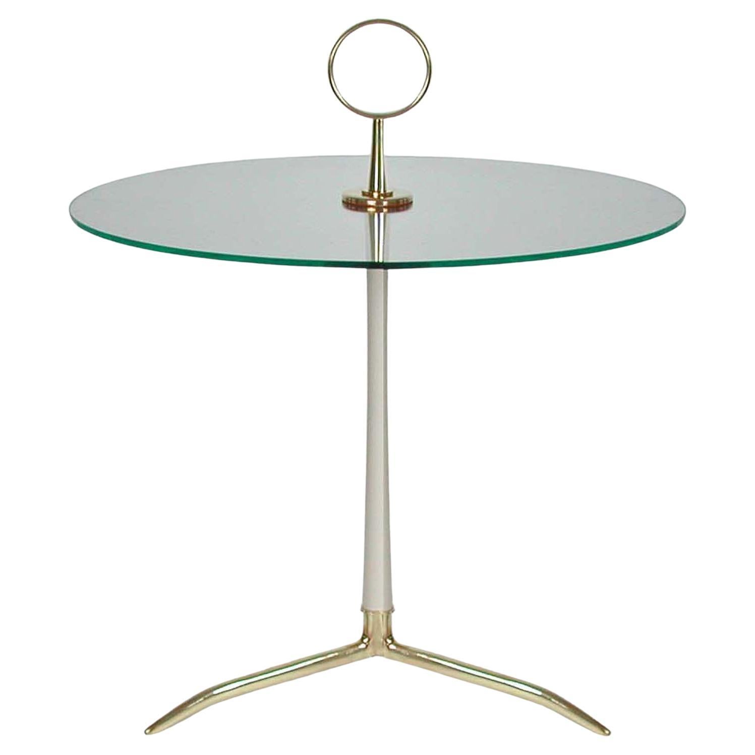 Dieser elegante, minimalistische Beistelltisch wurde in den 1950er Jahren in Deutschland von den Vereinigten Werkstätten München entworfen und hergestellt.

Sie besteht aus Messing, hellcremefarben lackiertem Metall und klarem Glas mit poliertem