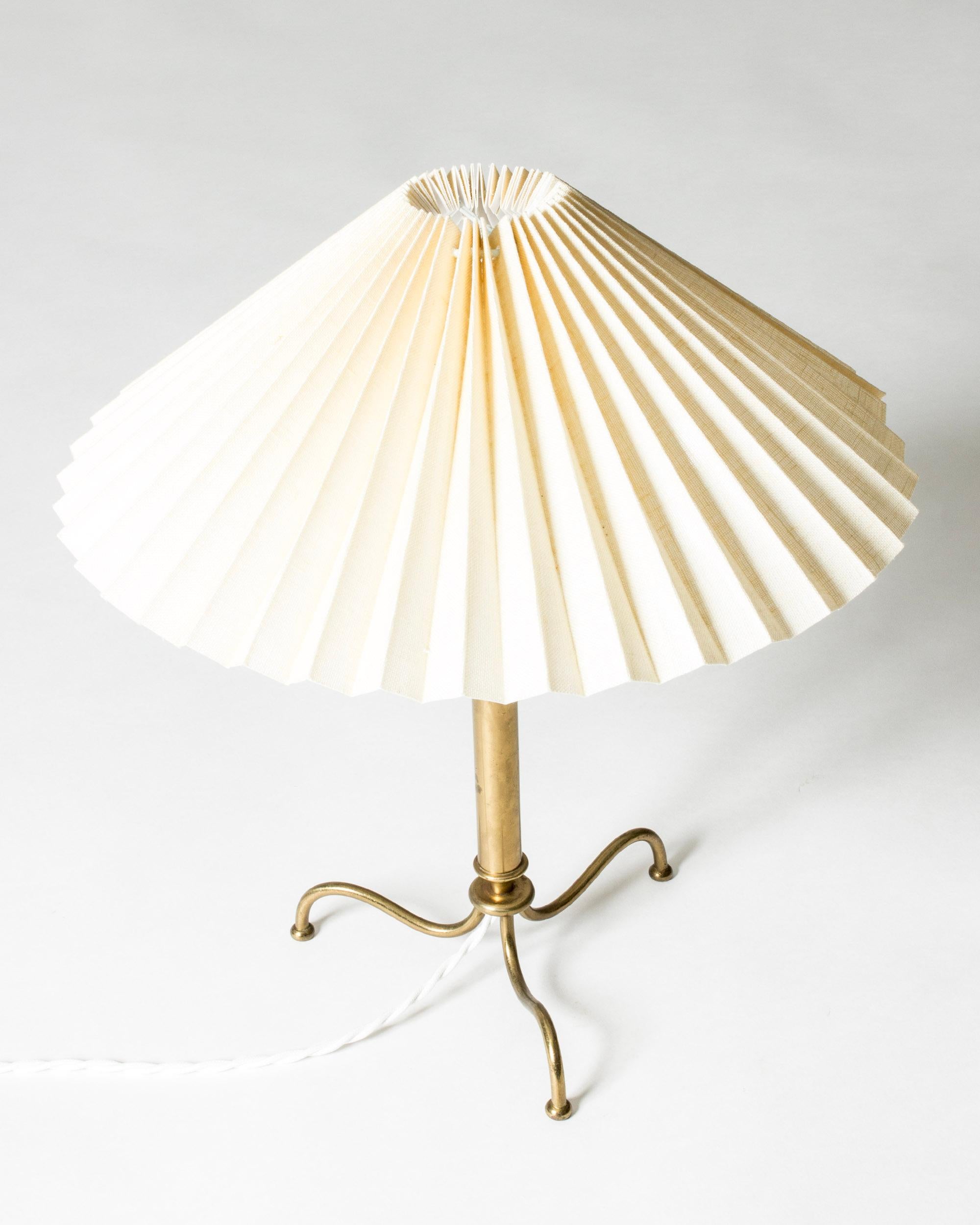 Charmante lampe de table suédoise moderne, en laiton, au design élancé avec trois pieds courbés. Abat-jour large et plissé.