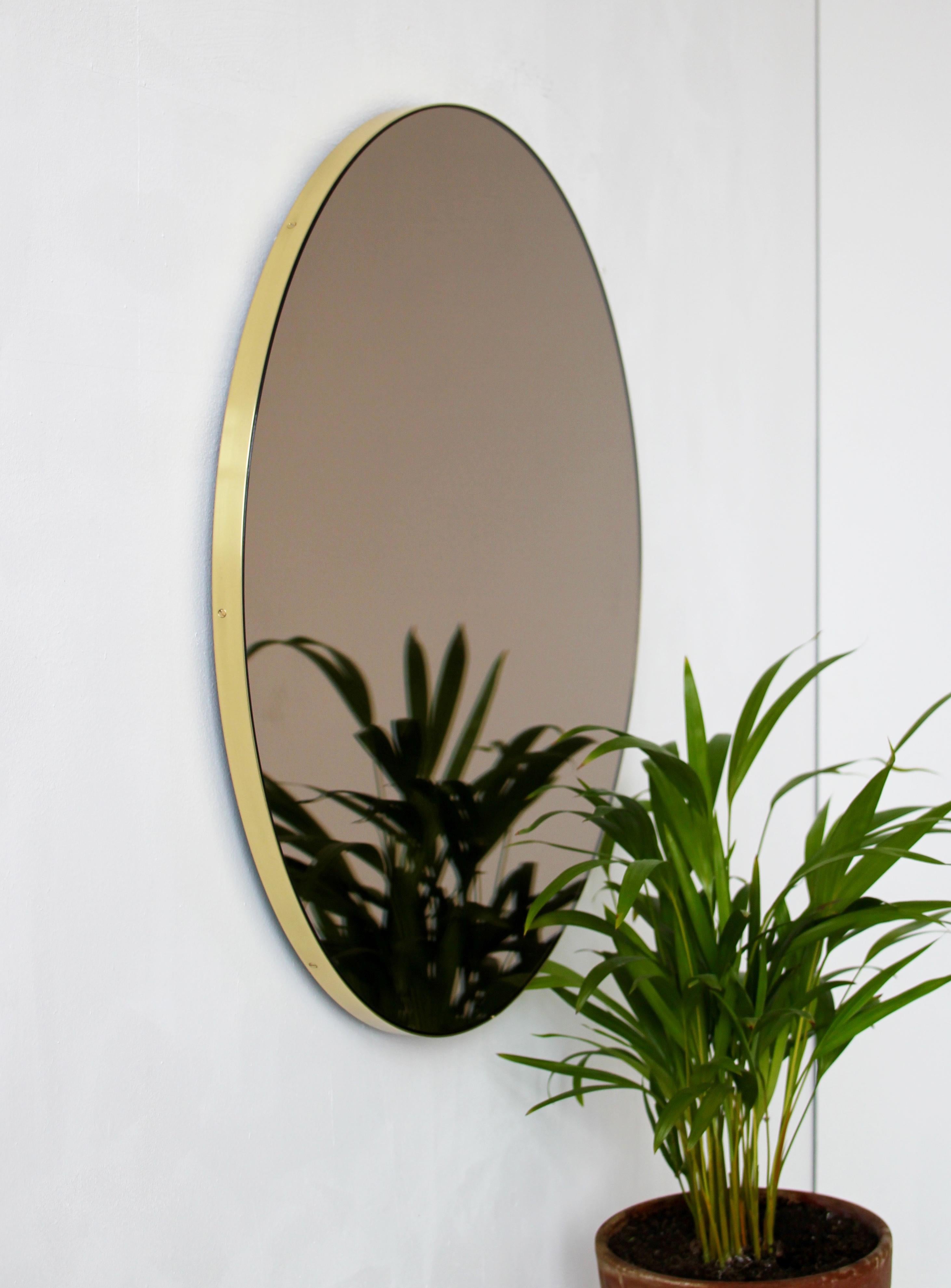 Minimalistischer, bronzefarbener, runder Spiegel mit einem eleganten Rahmen aus gebürstetem Messing. Die Details und die Verarbeitung, einschließlich der sichtbaren Messingschrauben, unterstreichen die handwerkliche Qualität des Spiegels, ein echtes