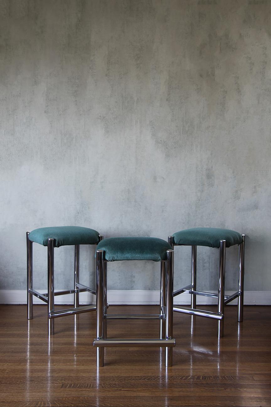 Introducing a set of three minimalist mid-century counter stools designed to add a touch of elegance to any kitchen or bar area. Each stool features sleek chrome legs that provide both durability and a modern aesthetic, while the vibrant turquoise