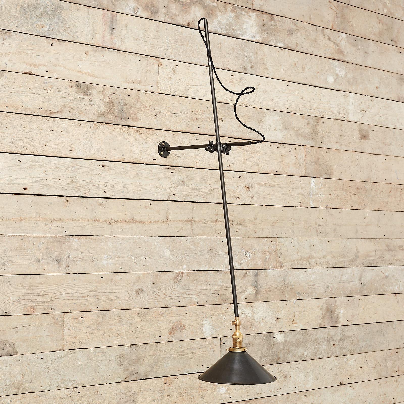 A well constructed modernist cantilever wall mounted light. The black enameled steel tube reaches out from the round wall mount. The decorative articulating mechanism is steel and the lamp holder and shade mount are in brass. The shade is black