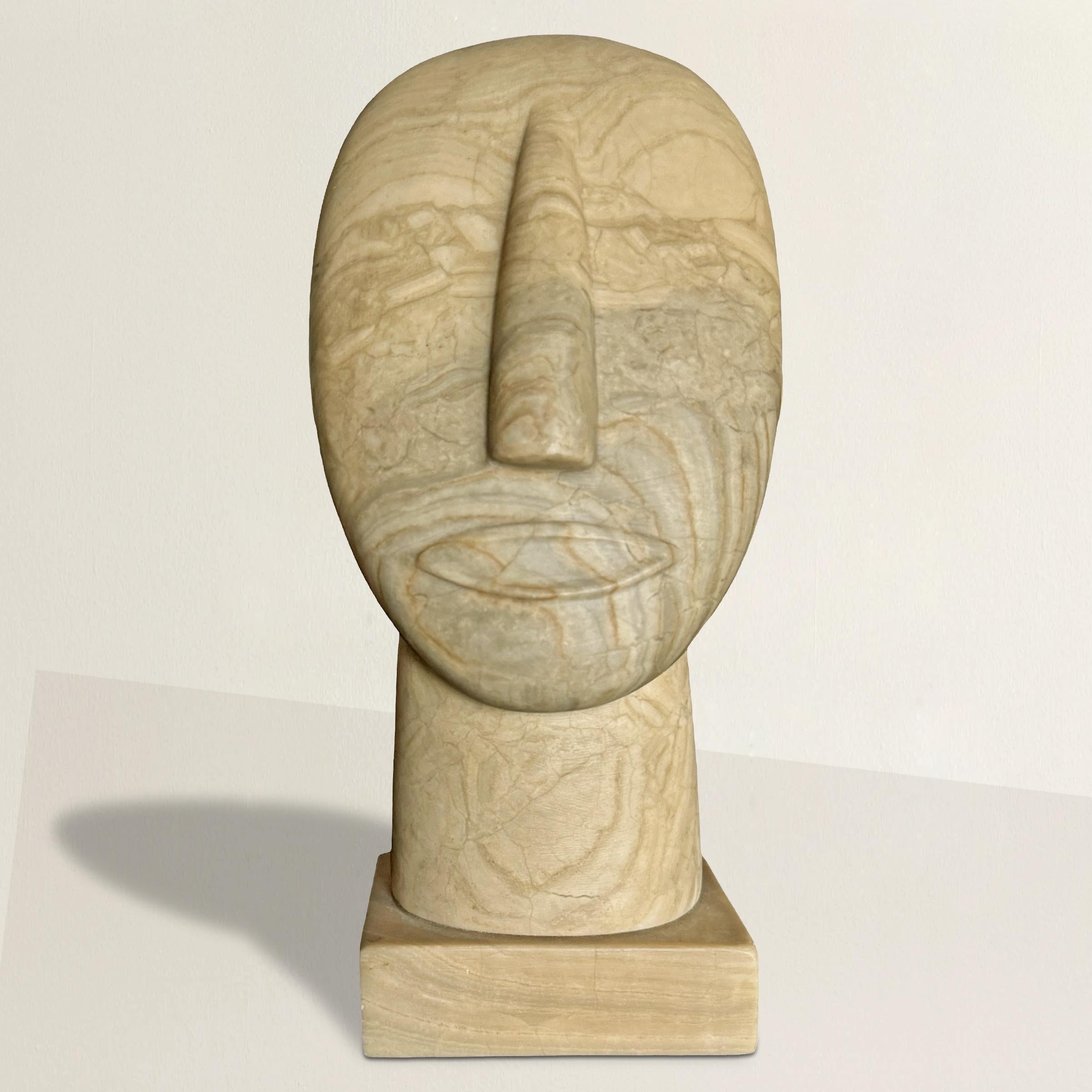 Este busto-retrato de piedra del siglo XXI, tallado a mano, está expertamente tallado en una piedra gris y tostada a rayas. El artista utilizó experta e intencionadamente el veteado natural de la piedra para formar los ojos, realzando la expresión