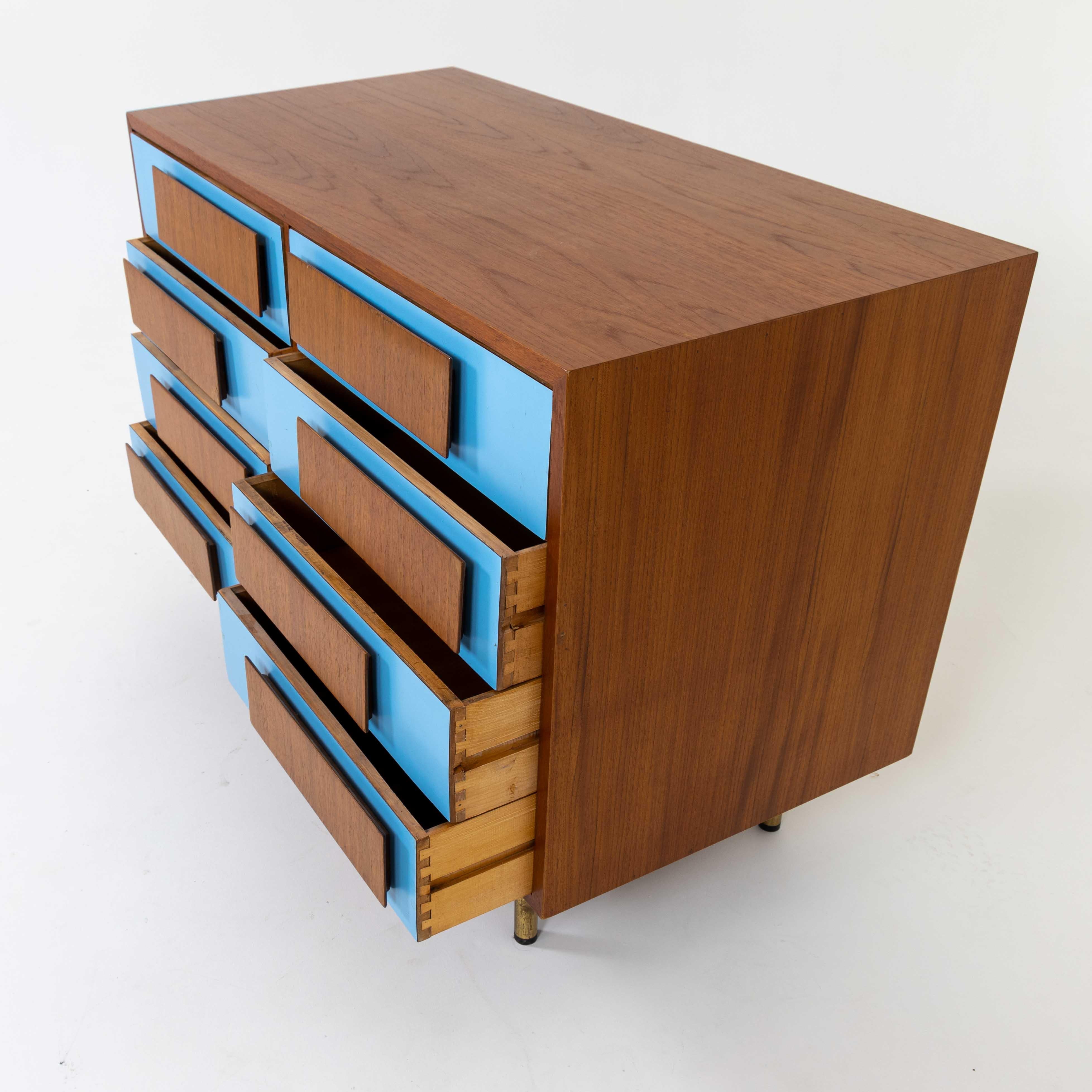 A modernist chest in the style of Gio Ponti. 
Veneer with decorative blue drawer fronts , patinated brass legs , and wood pulls.
