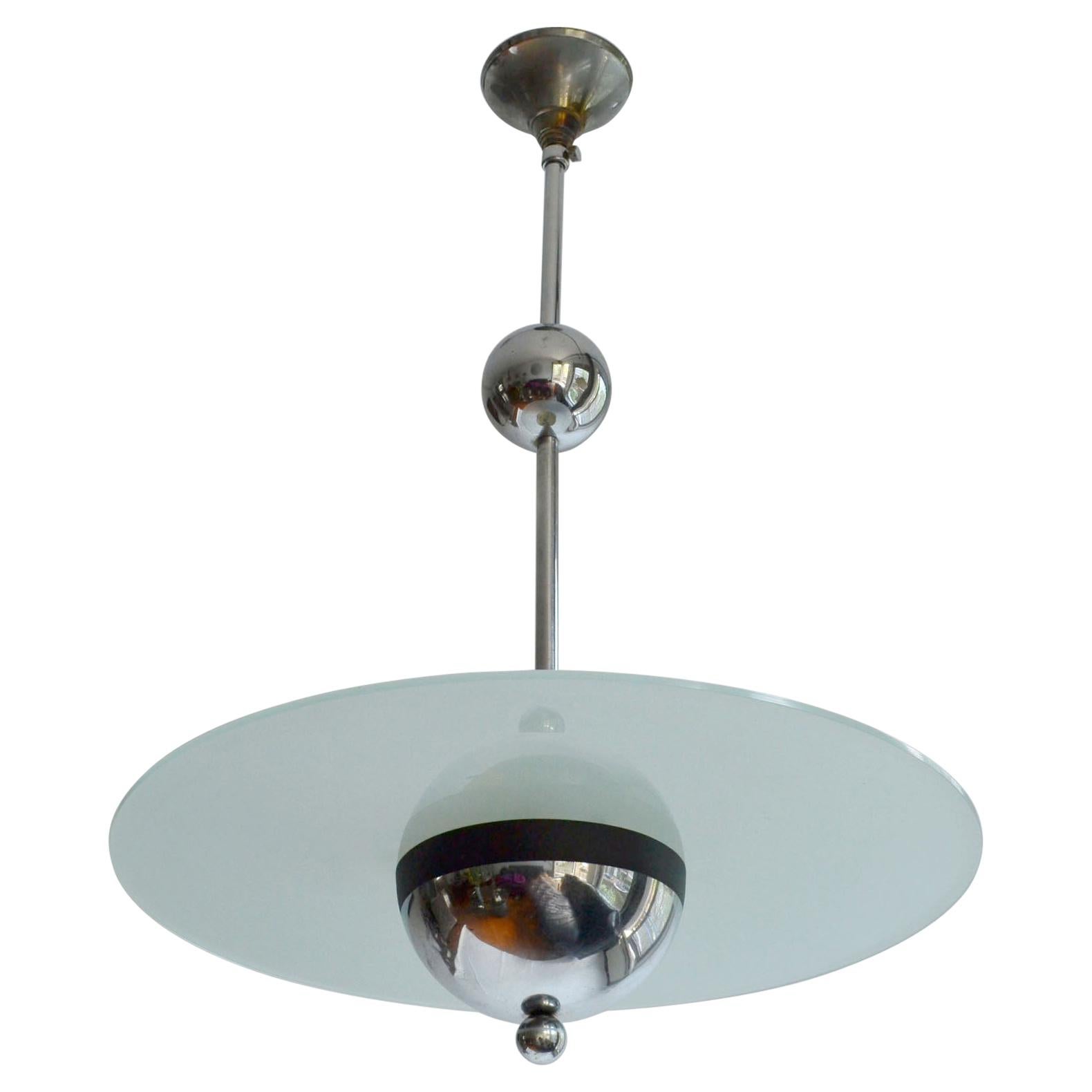 Art Deco pendant light in modernist style is in the style of Dutch Gispen lamps, possibly French or Belgium. The lamp is made of two elements, a chrome frame and a frosted glass disk simply resting on the half sphere that mirrors into the glass like