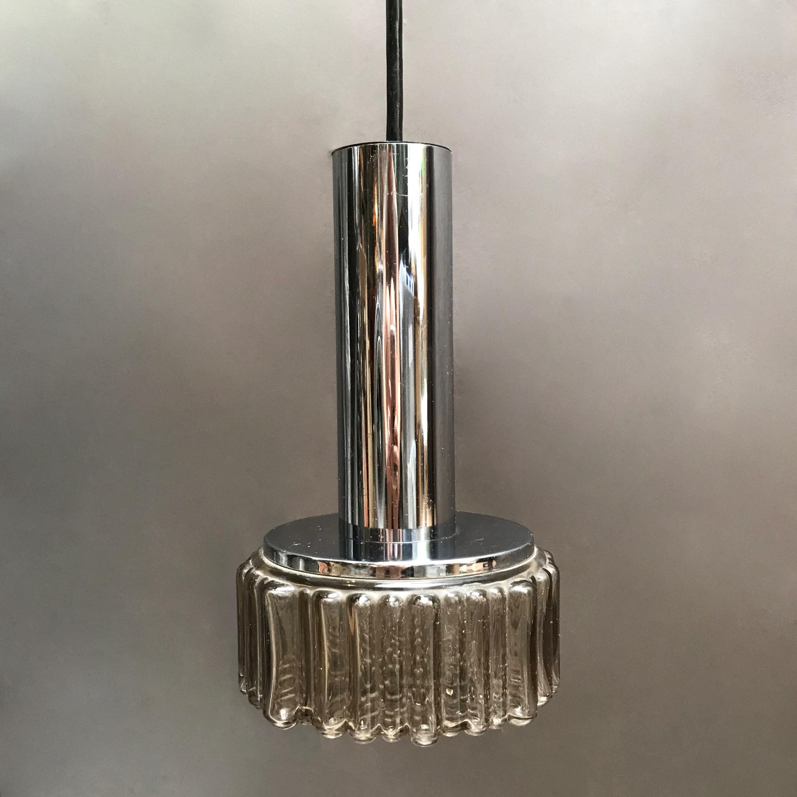 Modernist pendant light features a chrome cylinder with pebbled, smoked glass shade that measures 30 inches total height. With black cord and canopy.