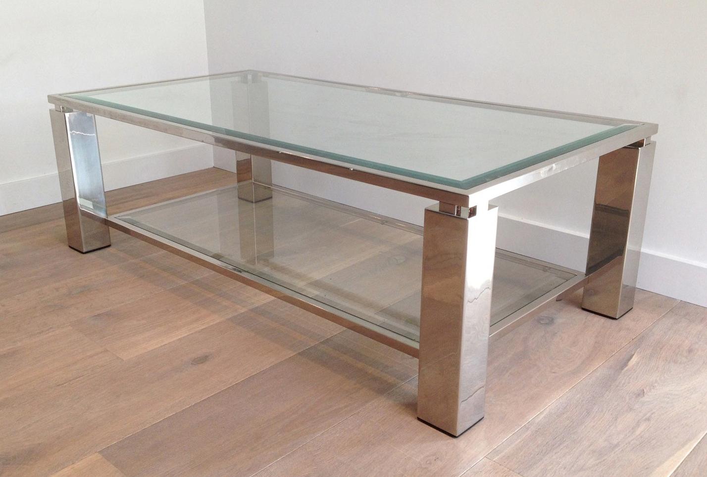This modernist coffee table is made of chrome with large square feet. It has 2 glass shelves, the top one which is beveled. This is a French work. Circa 1970.