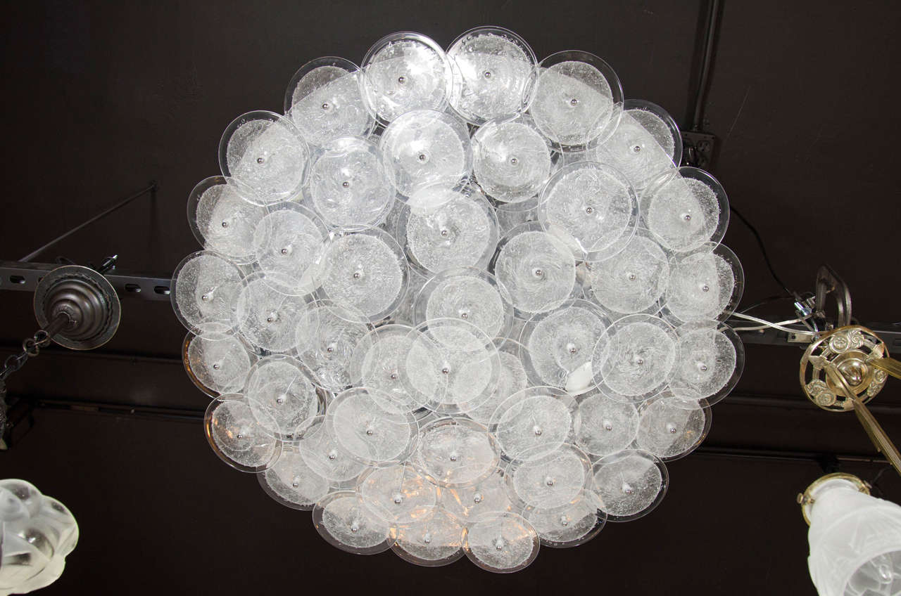 This stunning modernist chandelier was hand fabricated in Murano, Italy- the island off the coast of Venice renowned for centuries for its superlative glass production. It features an abundance of handblown Murano discs with translucent perimeters