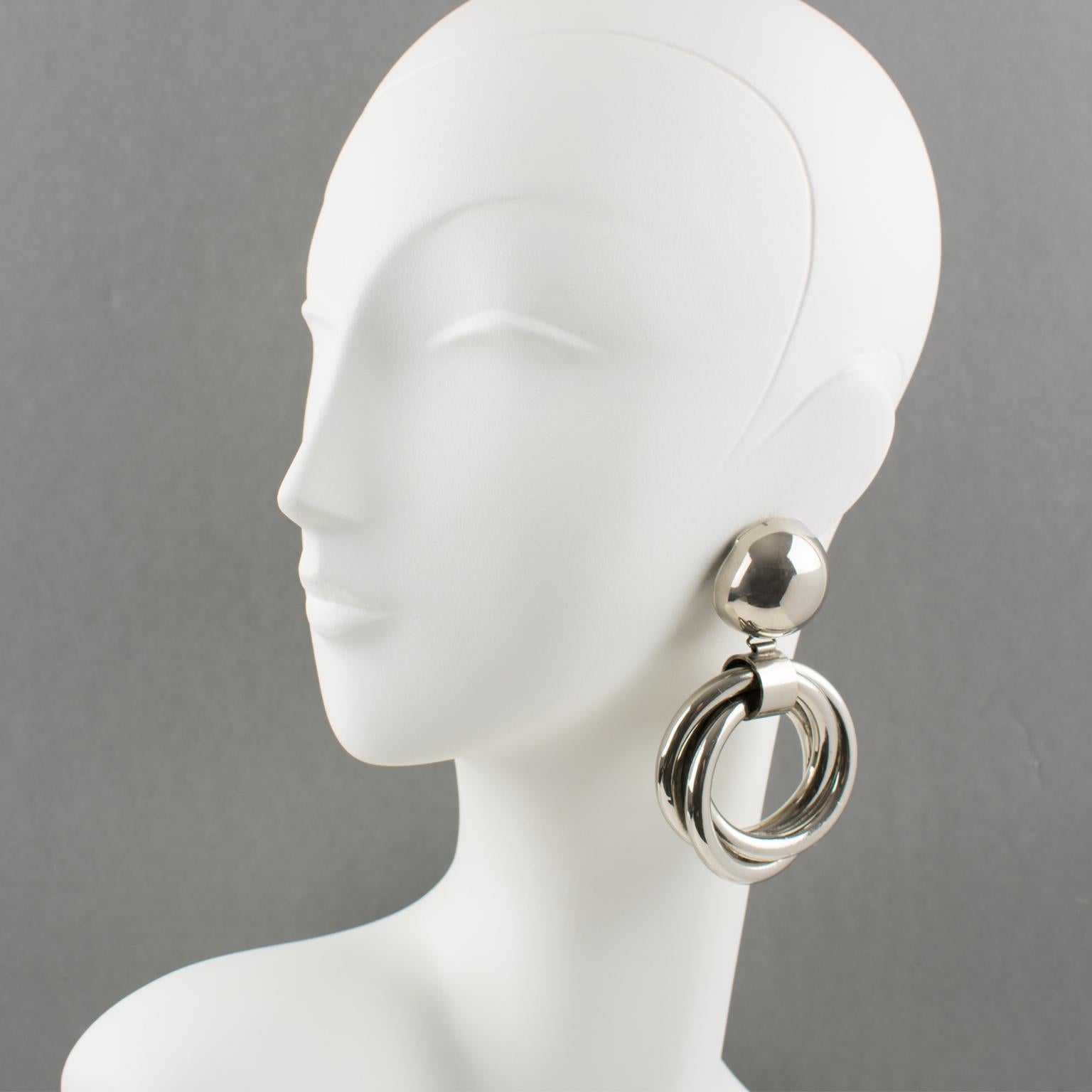 These stunning sculptural chrome metal clip-on earrings feature a geometric modernist dimensional dangling shape with a bold statement design. There is no visible maker's mark.
The earrings are in good condition, with a tiny bump on the side of the