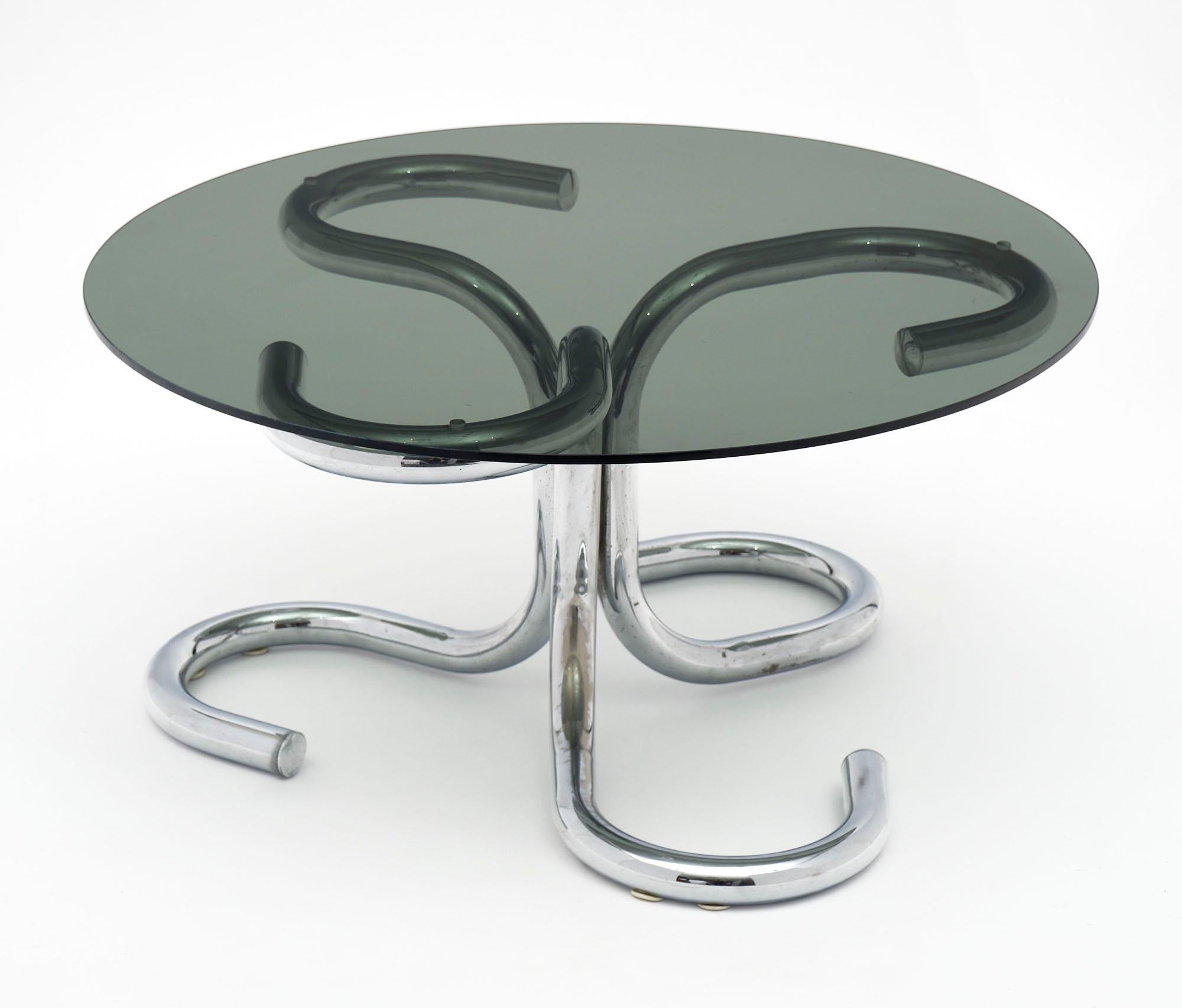 Sinuous chrome tube and glass coffee table in the spirit of Paul Tuttle’s “anaconda” coffee table for Strässle International. Three conjoining large diameter chrome tubes in a snake like design with chrome caps and a smoked glass top.