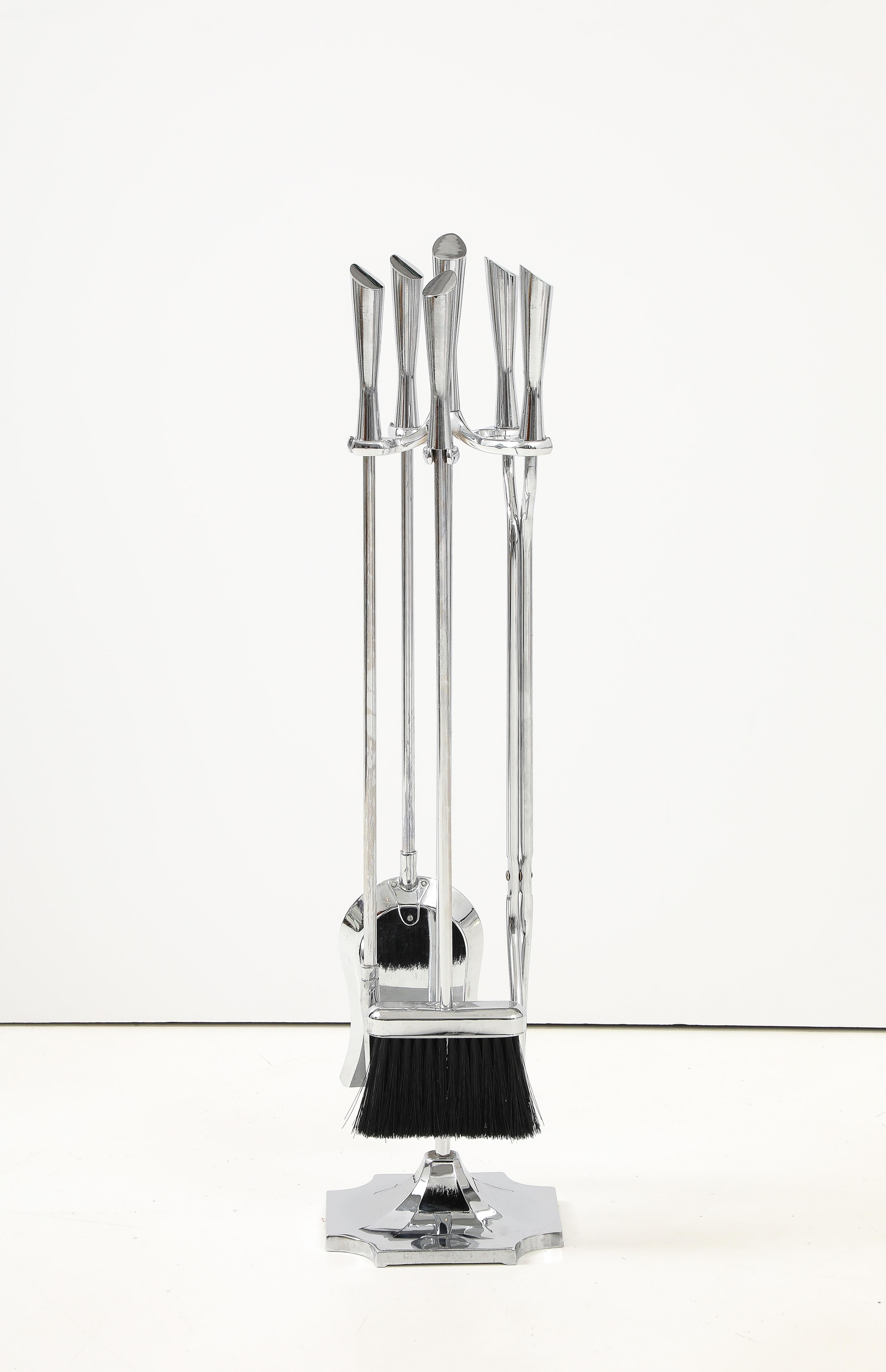 Ensemble d'outils pour le feu en acier lourd poli comprenant un support, un balai, une pelle, un tisonnier et une pince. Un ensemble moderne et élégant pour un décor contemporain.