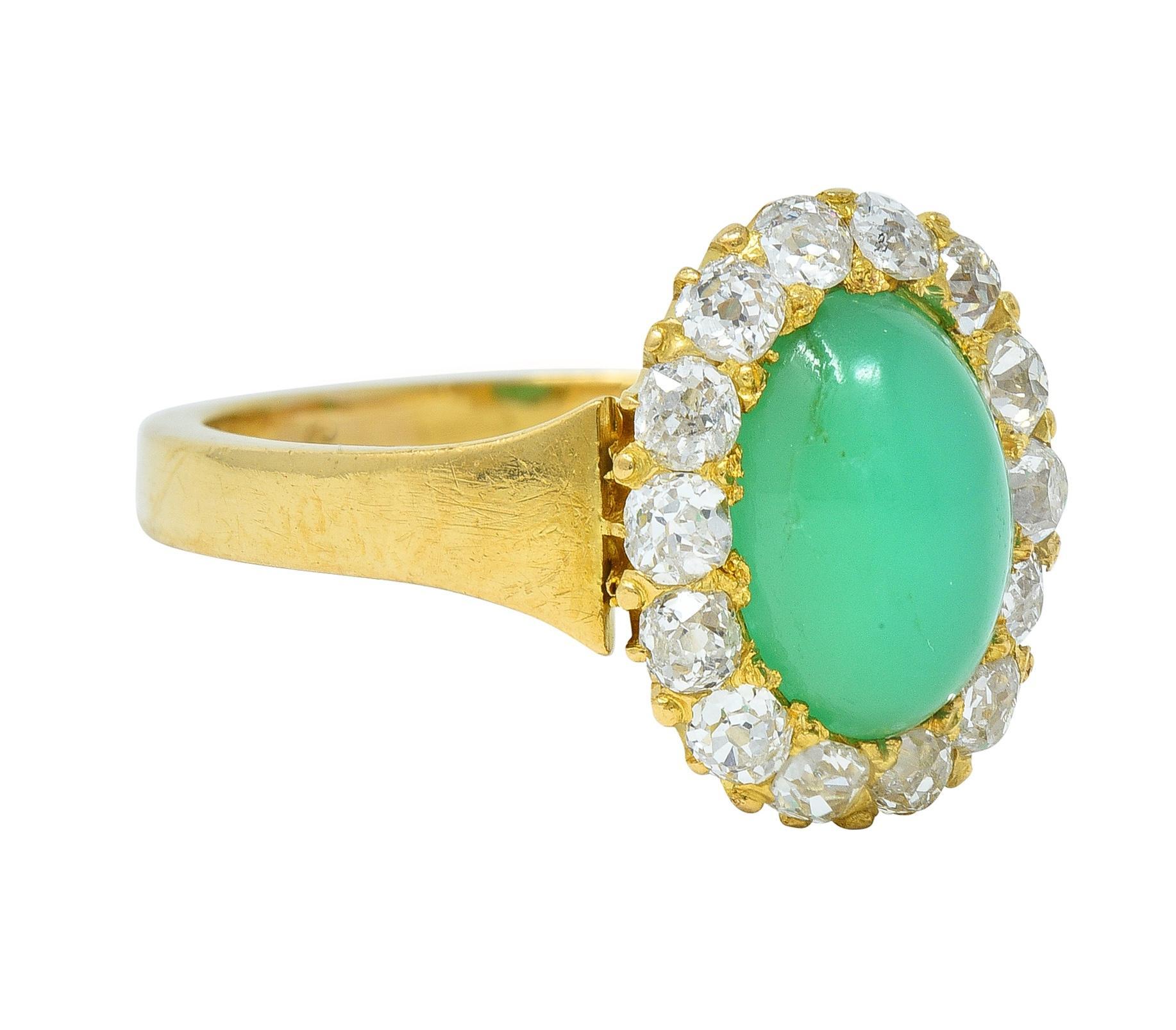 Centering an oval-shaped chrysoprase cabochon measuring 6.5 x 9.5 mm 
Translucent vibrant bluish green in color with subtle matrix 
Prong set with a halo surround of old mine cut diamonds 
Weighing approximately 0.42 carat total 
H to J color with