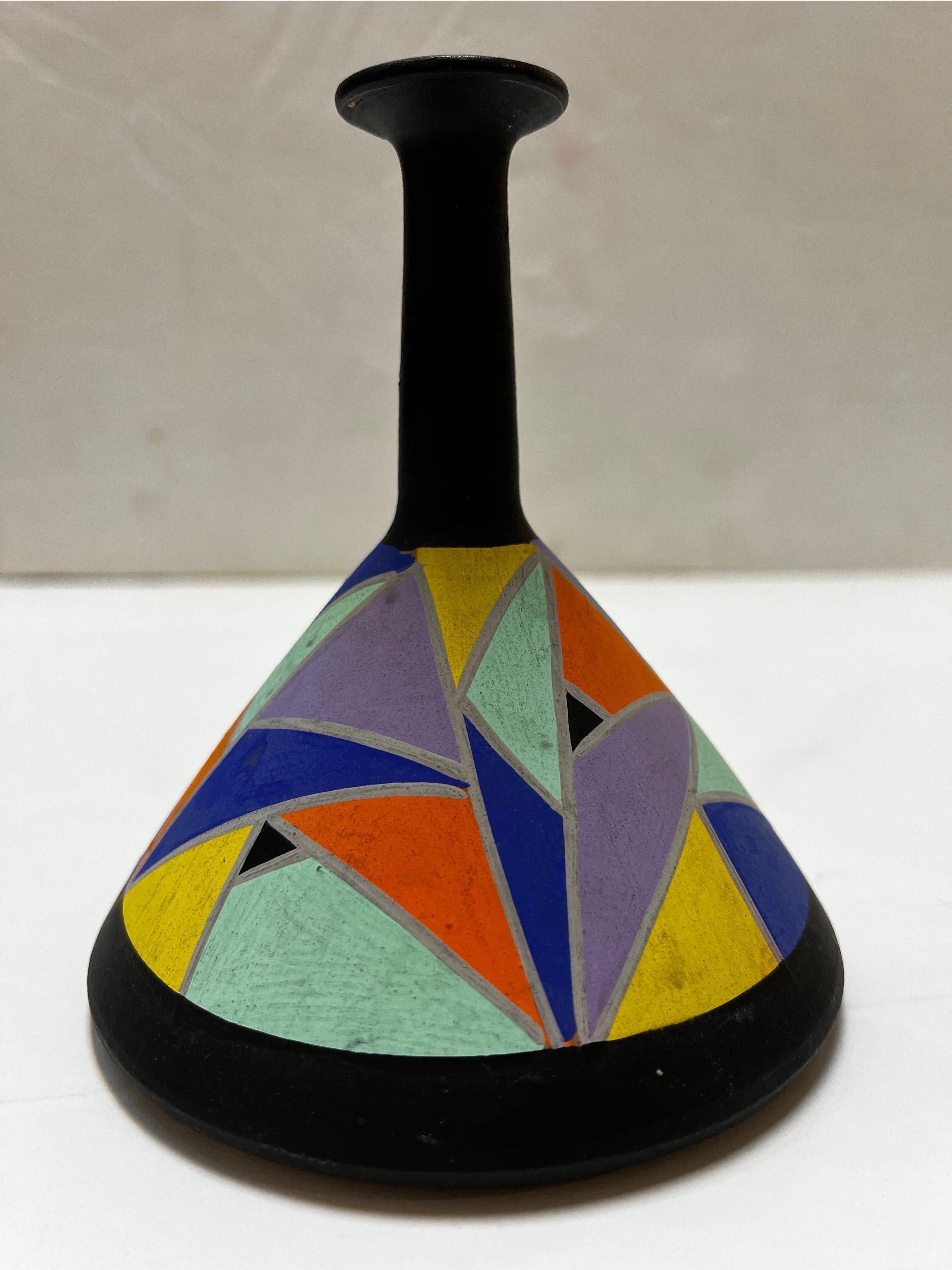 A vintage circa 1980's or 1990's hand painted pottery vase. The bold, geometric and Modernist style decoration is presented in full color against a black painted counterpoint. The conical base is accentuated by a slender elongated neck capped by the