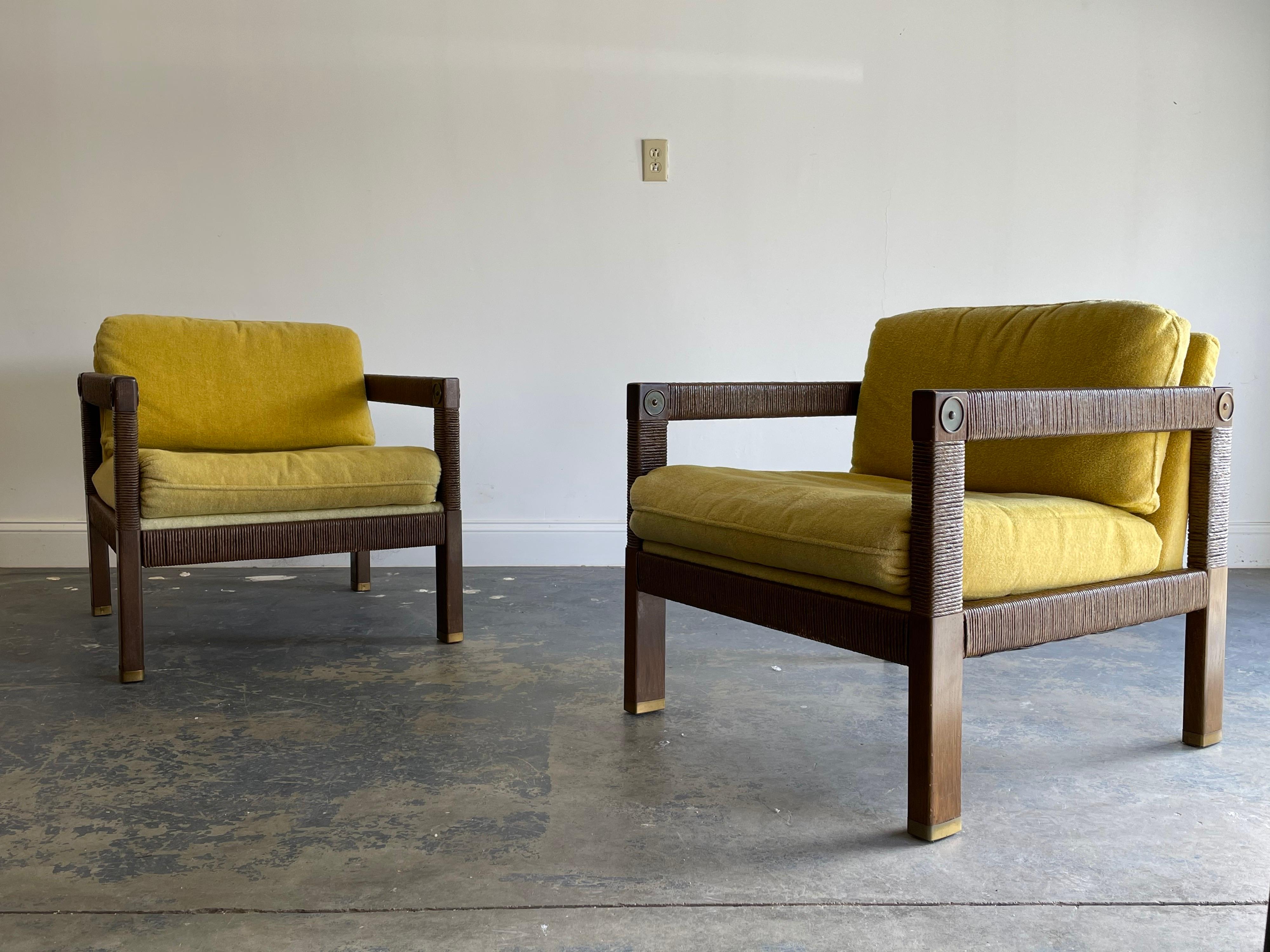 Unusual 1960s modernist club chairs with rush cord wrapped frame. Brass details at the ends of the arms, and brass capped feet. Use of organic materials would help these blend in a variety of interiors. Light and tasteful wear in an appealing nature.