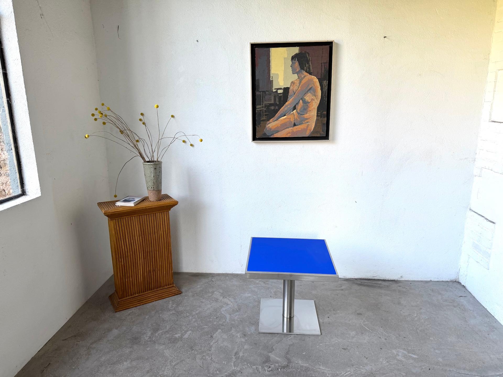 La Maison LECAN présente une table basse moderniste des années 1970, au design audacieux et minimaliste.
Il se compose d'un plateau carré en stratifié bleu vif, encadré d'acier brossé, reposant sur une base centrale en métal tubulaire dotée d'un