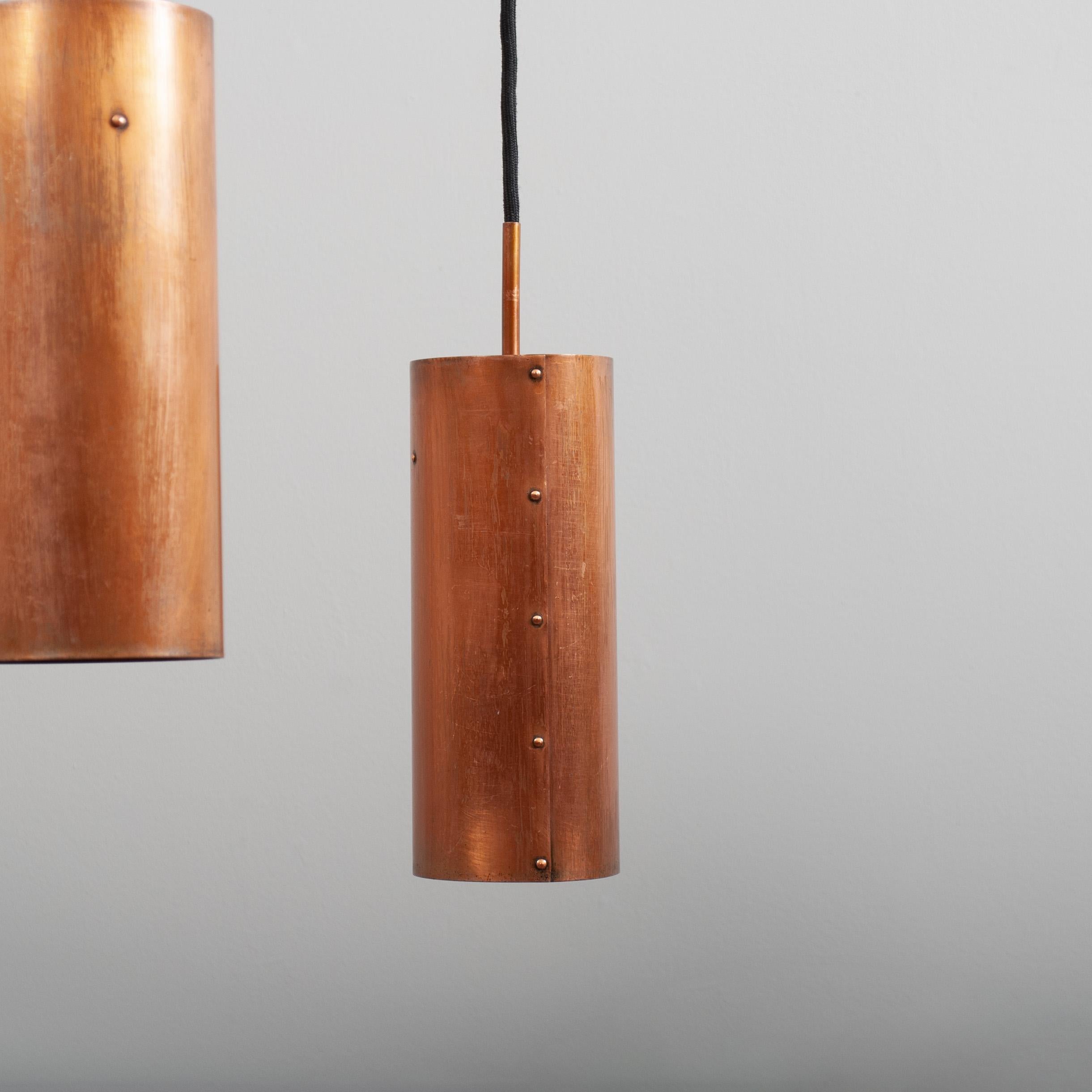 An idiosyncratic handcrafted Modernist Danish triple drop pendant light. Constructed from solid copper with a curved copper yoke which suspends 3 riveted copper cylinders - by moving the yoke up/down these can be a graduated drop or lined up level