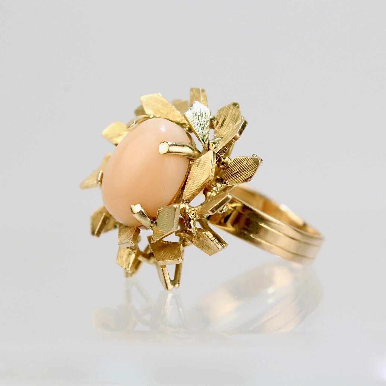 A very fine coral and 14k gold floral ring.

With a pink or peach colored oval coral cabochon prong center set and surrounded by 14 karat gold leaf patterns.

Date:
20th Century

Overall Condition:
It is in overall good, as-pictured, used estate