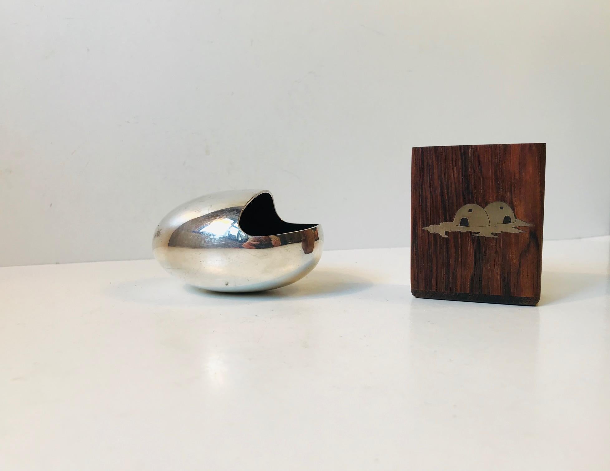 A midcentury set consisting of the smile ashtray by Carl Cohr and a cigarette holder by Axel Salomonsen. The ashtray is made from silver plated brass and the cigarette holder from sterling silver inlaid wood. Both pieces are Danish and date from the