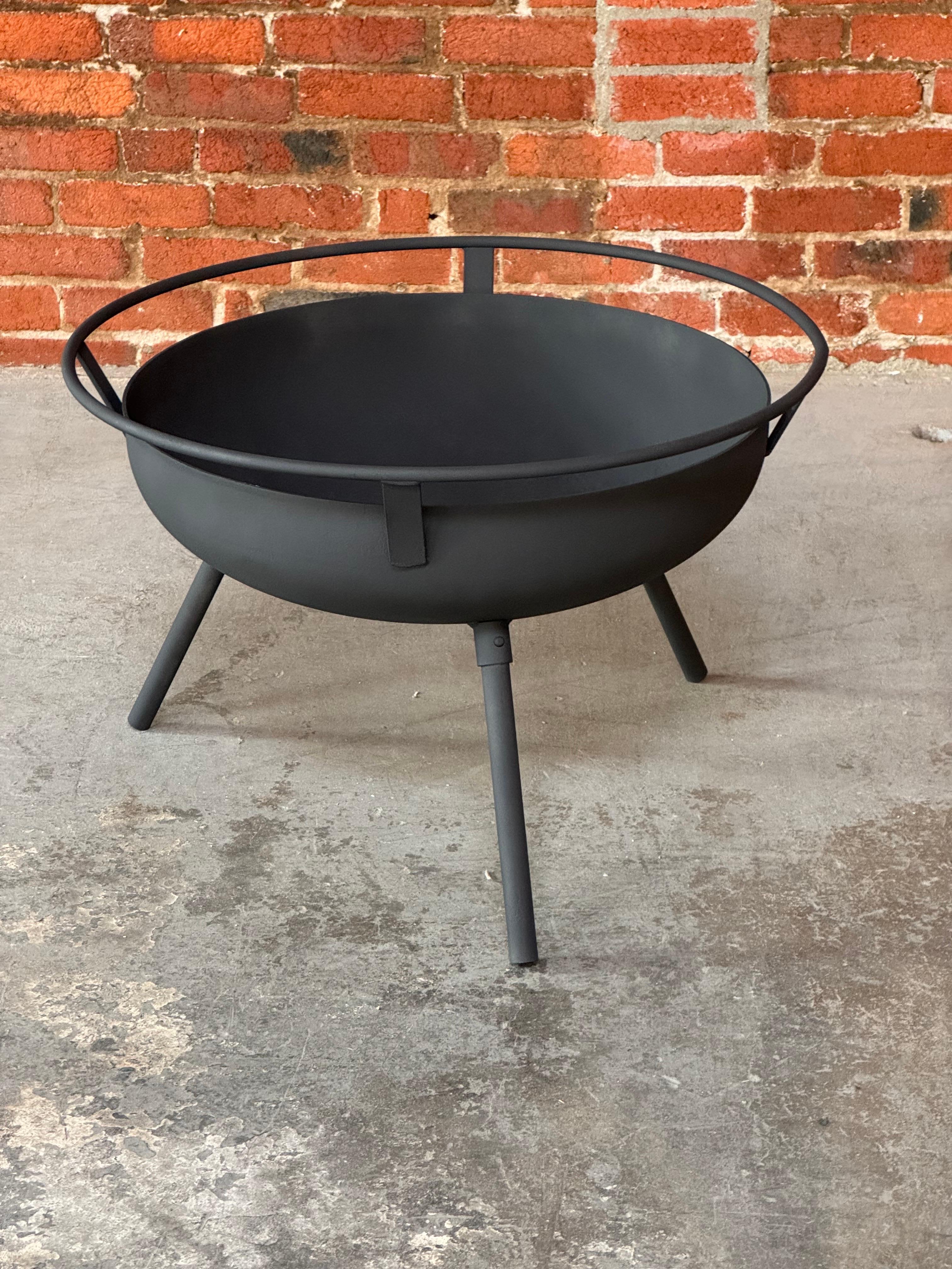 Modernist design circa 1950s three legged iron fire pit. Consisting of a thick iron bowl with a welded iron ring intended as a handle attached to the outside rim of the fire pit and is supported by three detachable tubular iron legs. The fire pit