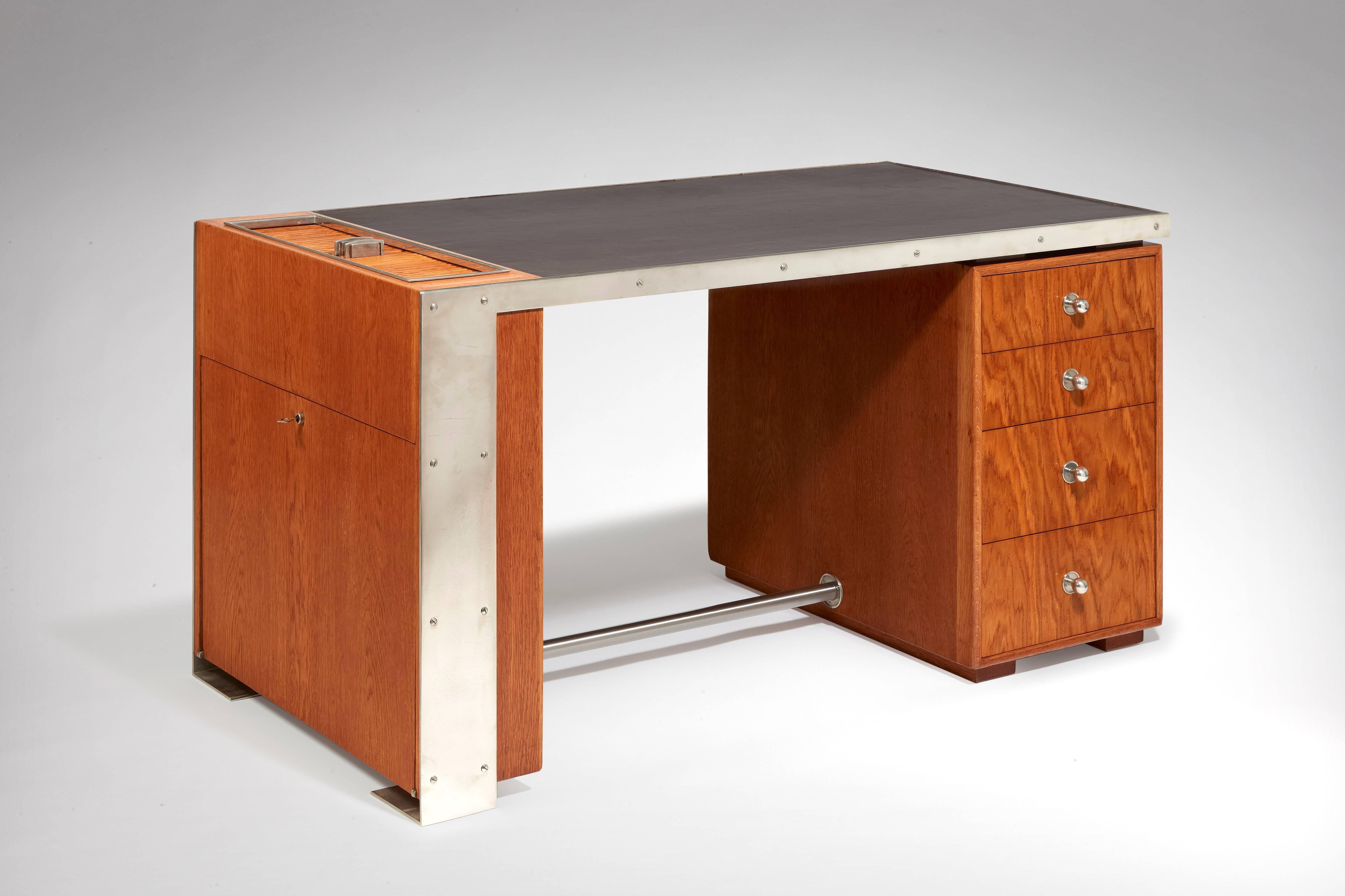 Asymmetrical modernist desk with an oak veneer and nickel-plated metal structure composed in the right part by a box opening on four drawers, in the left part a box opening at the top by a cabinet with sliding-doors closure and laterally by
a