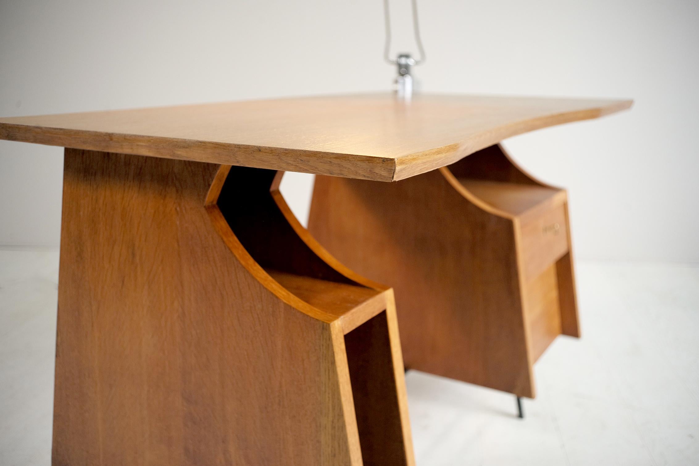 Bureau in blond oak and black lacquered tubular iron legs, attributed to Henri Lancel, France, 1950. Trapezoid-shaped pedestals have on one side two drawers, one lockable, and on the other an open storage space. The tray is slightly hollowed out in