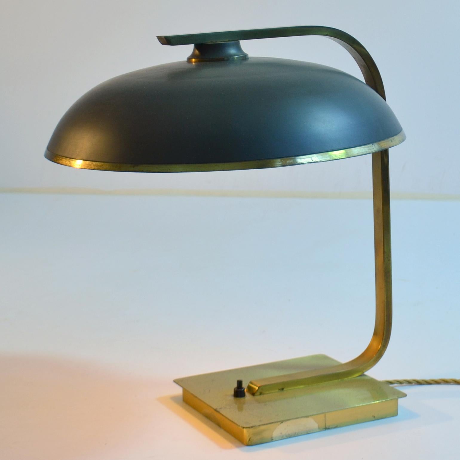 Modernist brass desk lamp with patinated brown round shade edged in shiny brass is held on a brass angular arm that connects to a square brass base in the style of Bauhaus is made in the 1950's.