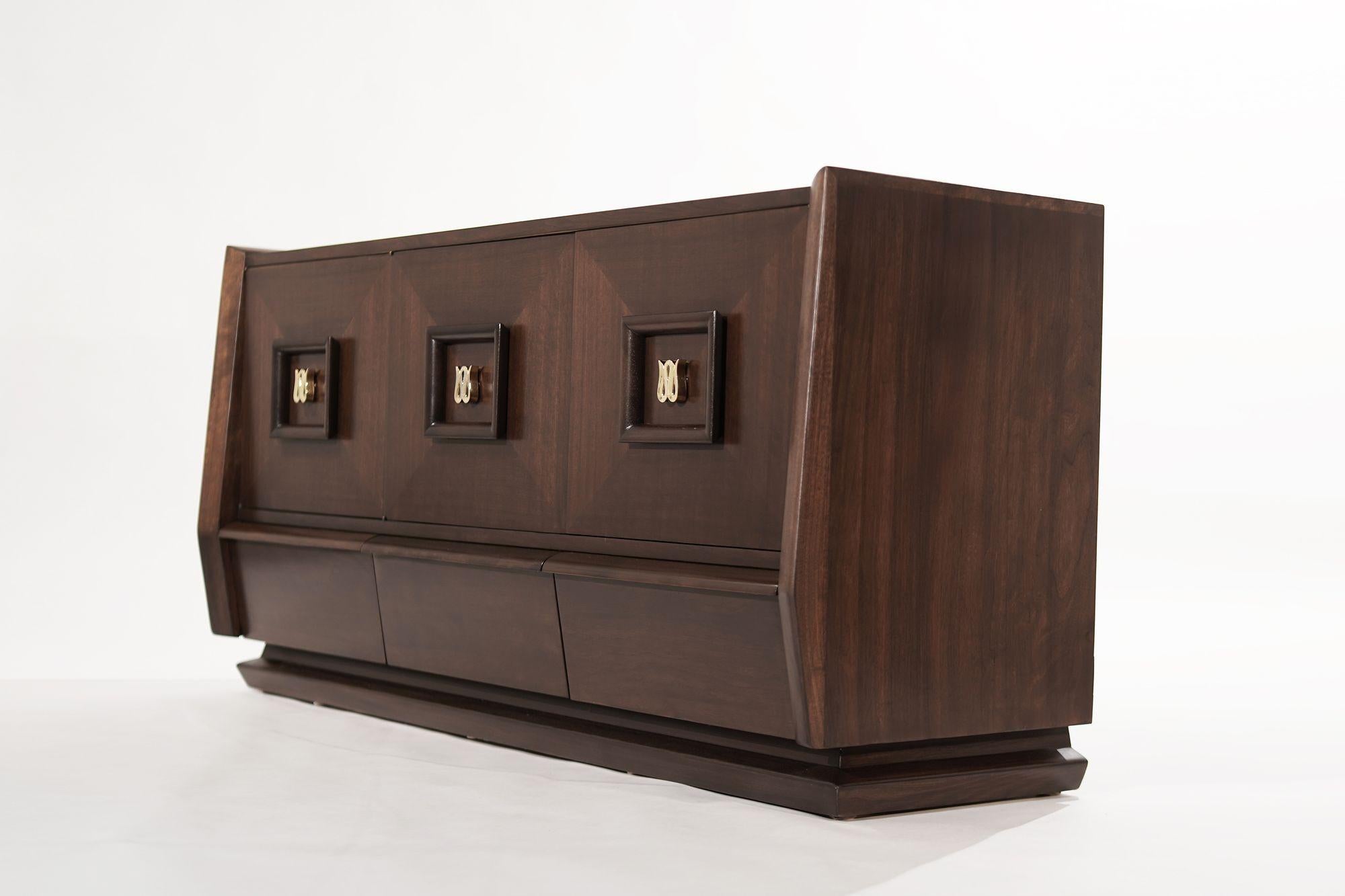 A walnut dresser original from Italy, circa 1950-1959. Featuring swooping curves and sudden edges, the three doors open up to reveal 6 large drawers with an additional 3 drawers underneath providing ample storage space. Hand-polished brass 
