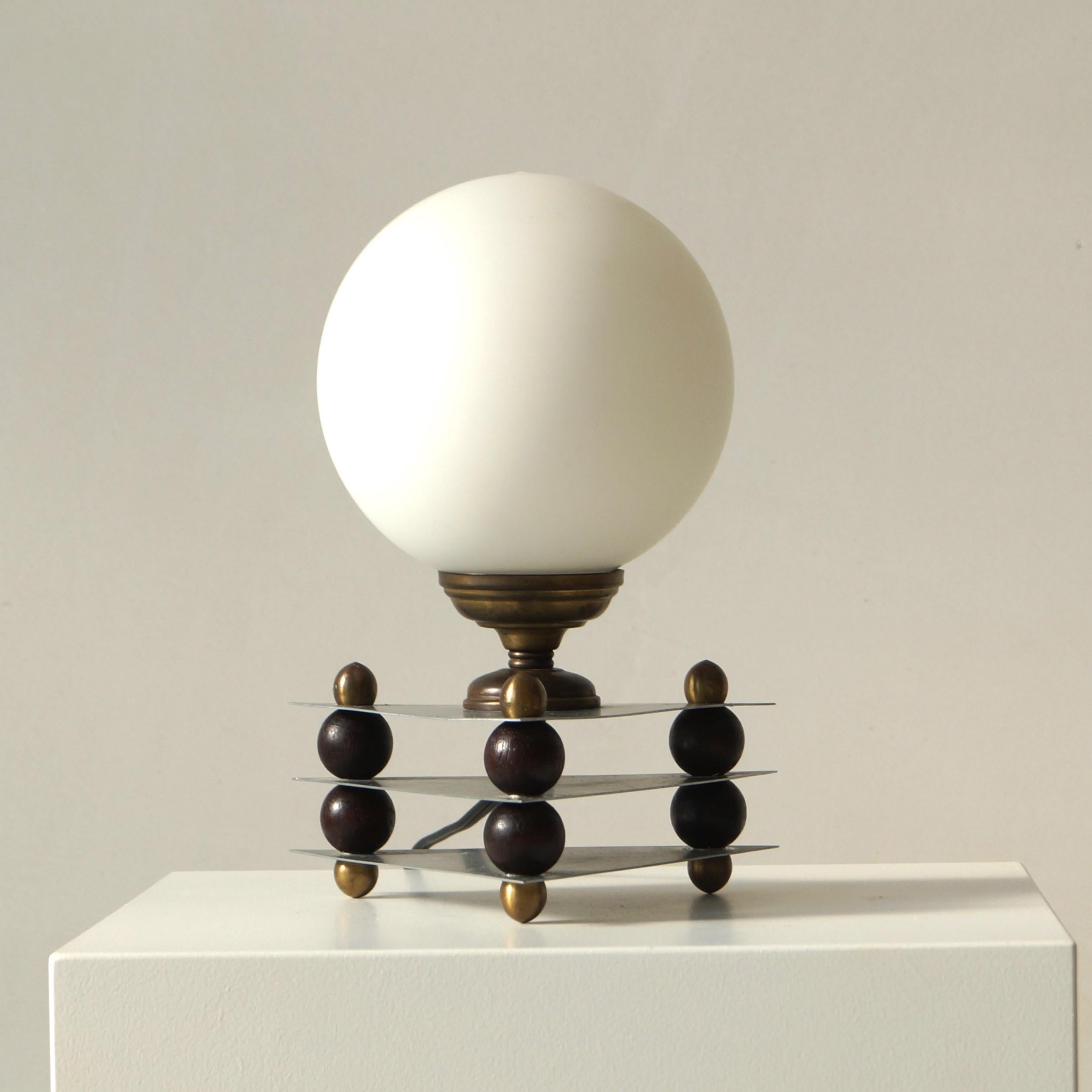 A decorative table lamp with a modernist geometric design. As the wiring is around 1950s, we dated the lamp at 1950. It is possibly older.
The stylish lampbase consists of two triangular metal plates  with in between them, small wooden balls and a