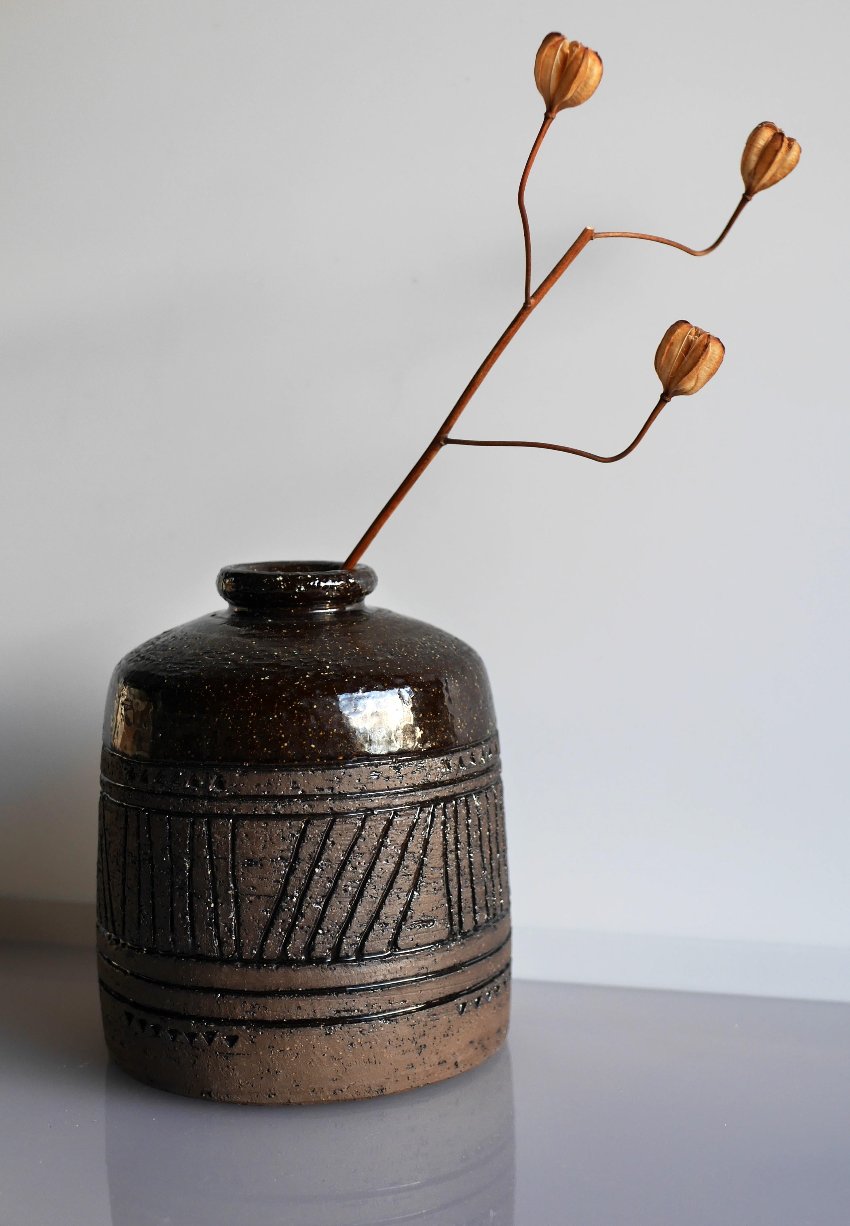A stunning, dark, heavy piece from Inger Persson for Rörstrand, Sweden. A dark brown earthenware base with a primitive style of pattern with lines and triangles scored around the sides. The shoulders and neck have a deep brown glaze. As usual from