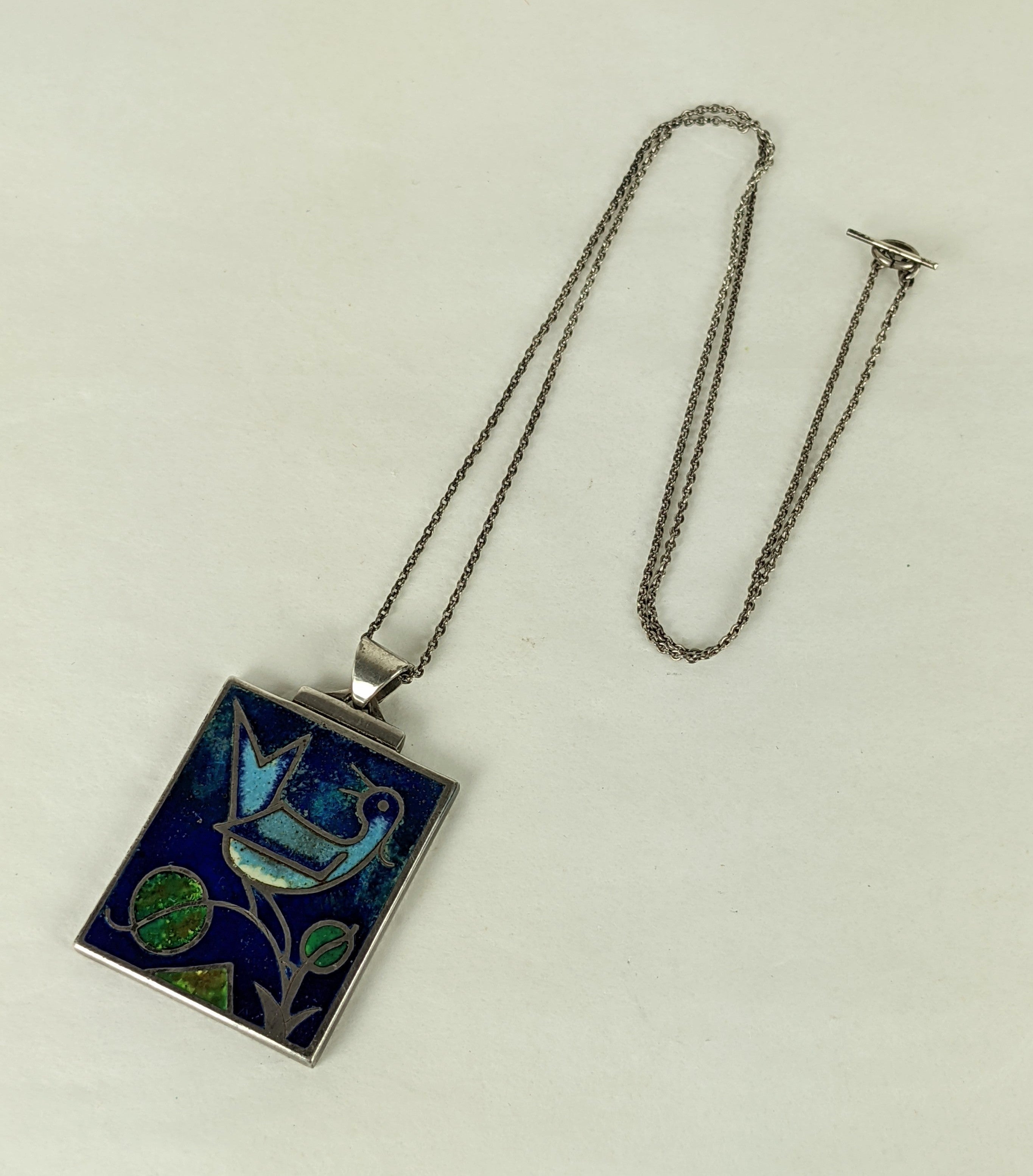 Elegant Modernist Enamel Pendant from Germany circa 1940's. Charming matte enamel bird on branch in cobalt, sky blue and green in a stepped Deco sterling setting with original 