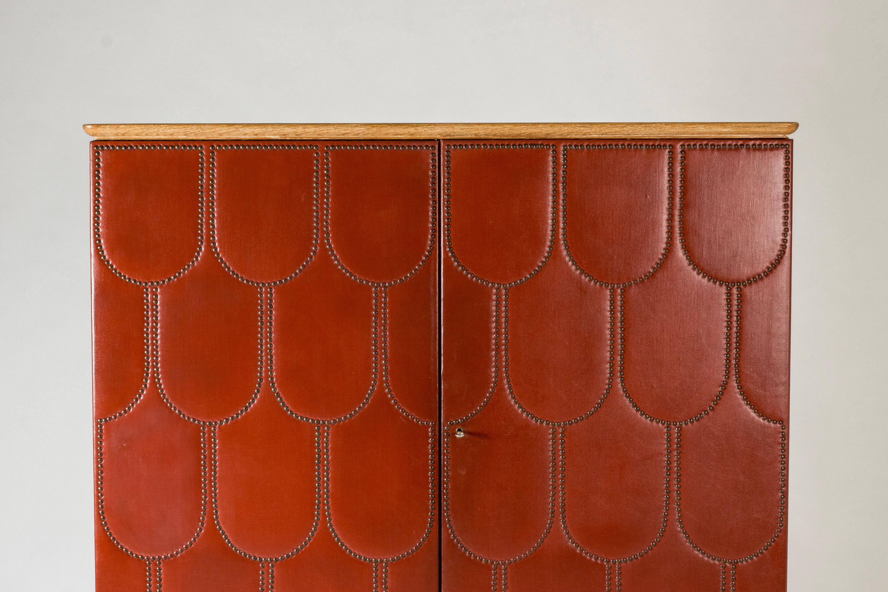 Amazing cabinet by Otto Schulz, in a bold design with oxblood colored faux leather front and sides. Decor of brass nails in a graphic pattern. White washed oak legs.