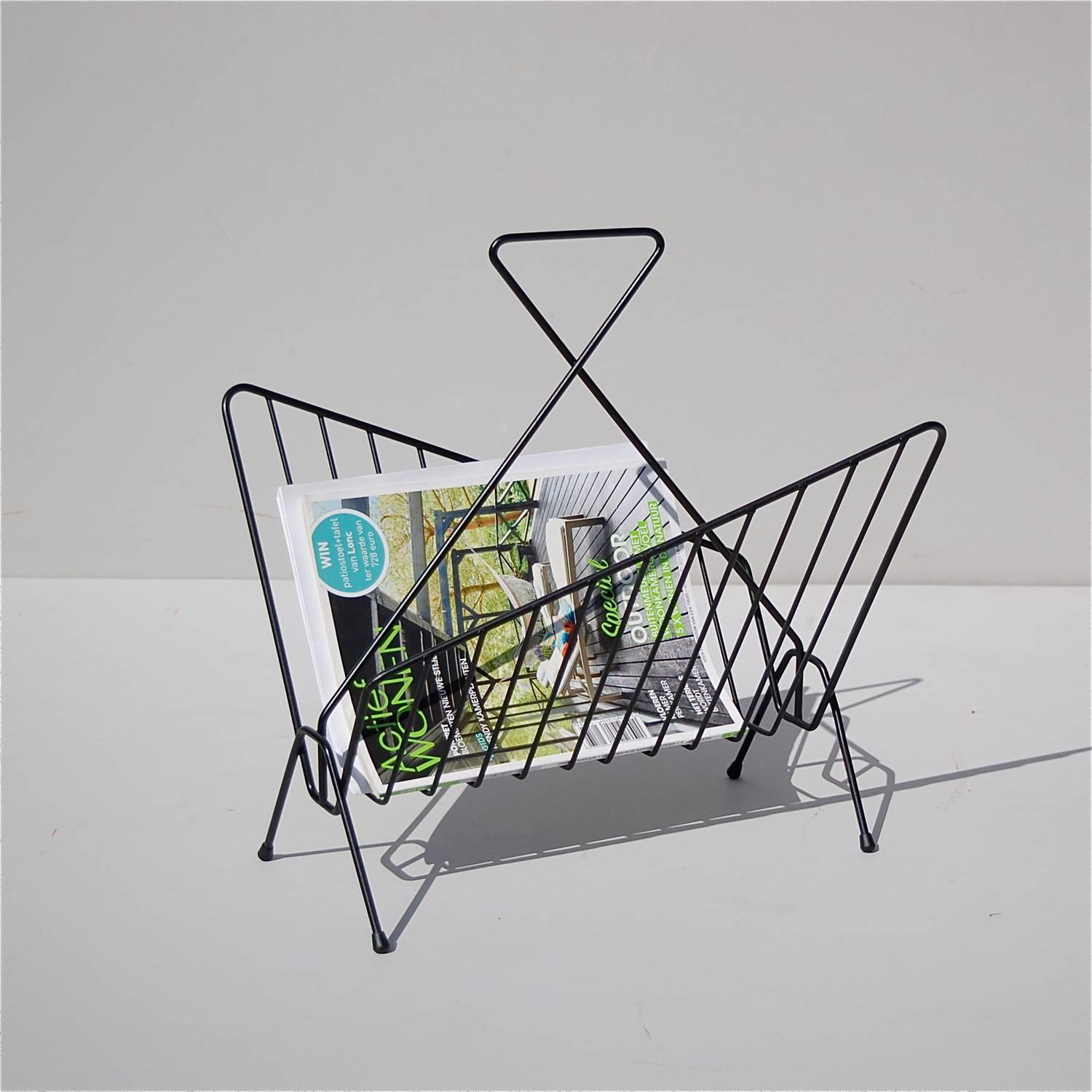 Mid-20th century geometric shaped magazine rack or newspaper holder in black lacquered metal. The trapezium shape of the side supports is identical, but in mirror image of each other. This creates a visually interesting and eye-catching effect. The