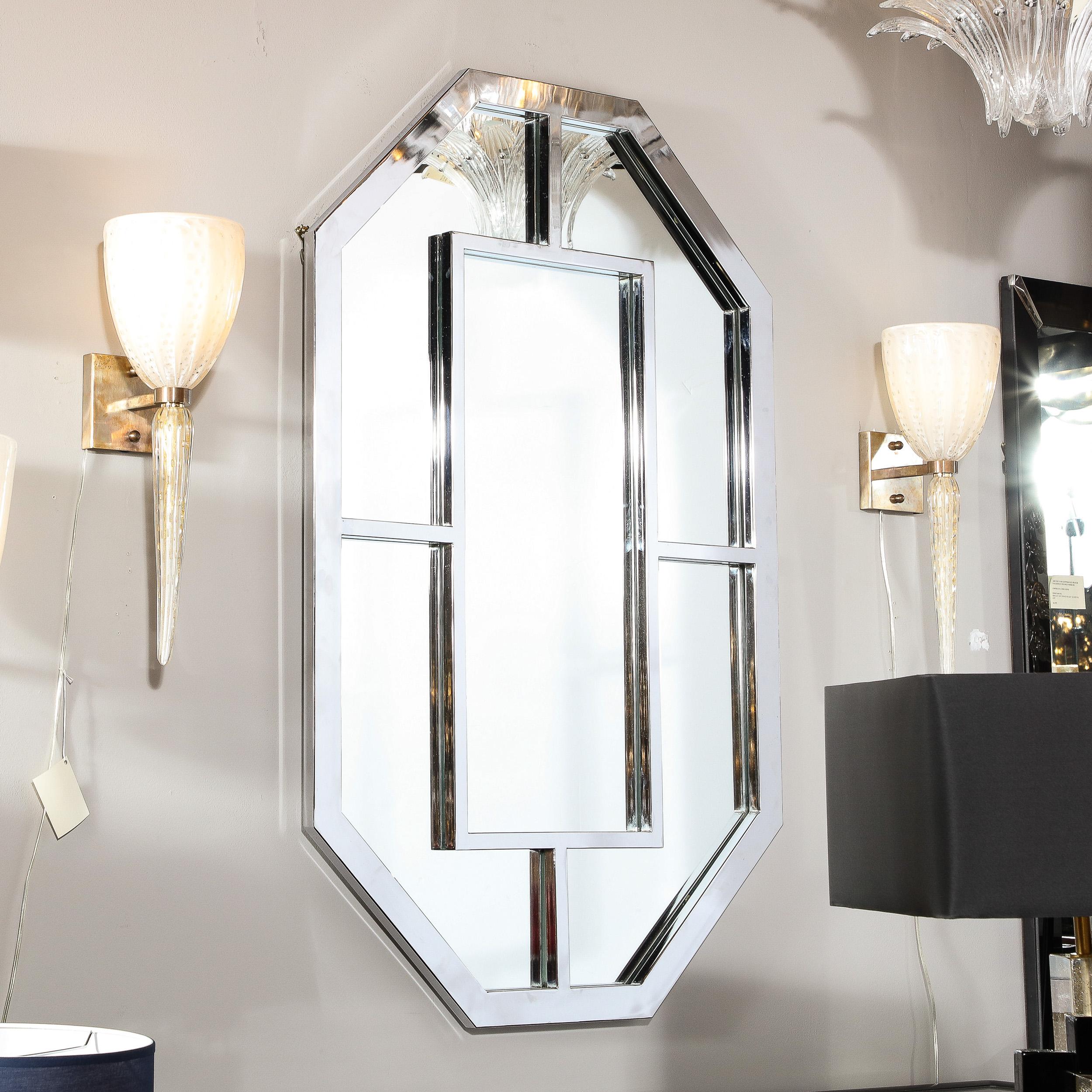This stunning Mid Century Modern mirror was realized in The United States circa 1970. It offers an octagonal silhouette circumscribed in polished chrome with an open form square embellishment in the center connected to the exterior via volumetric
